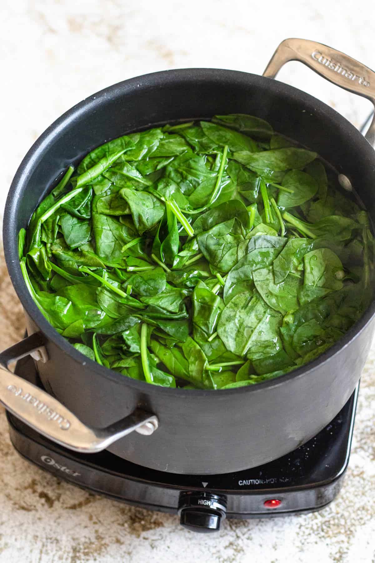 Spinach being blanched in hot water in a saucepan. 