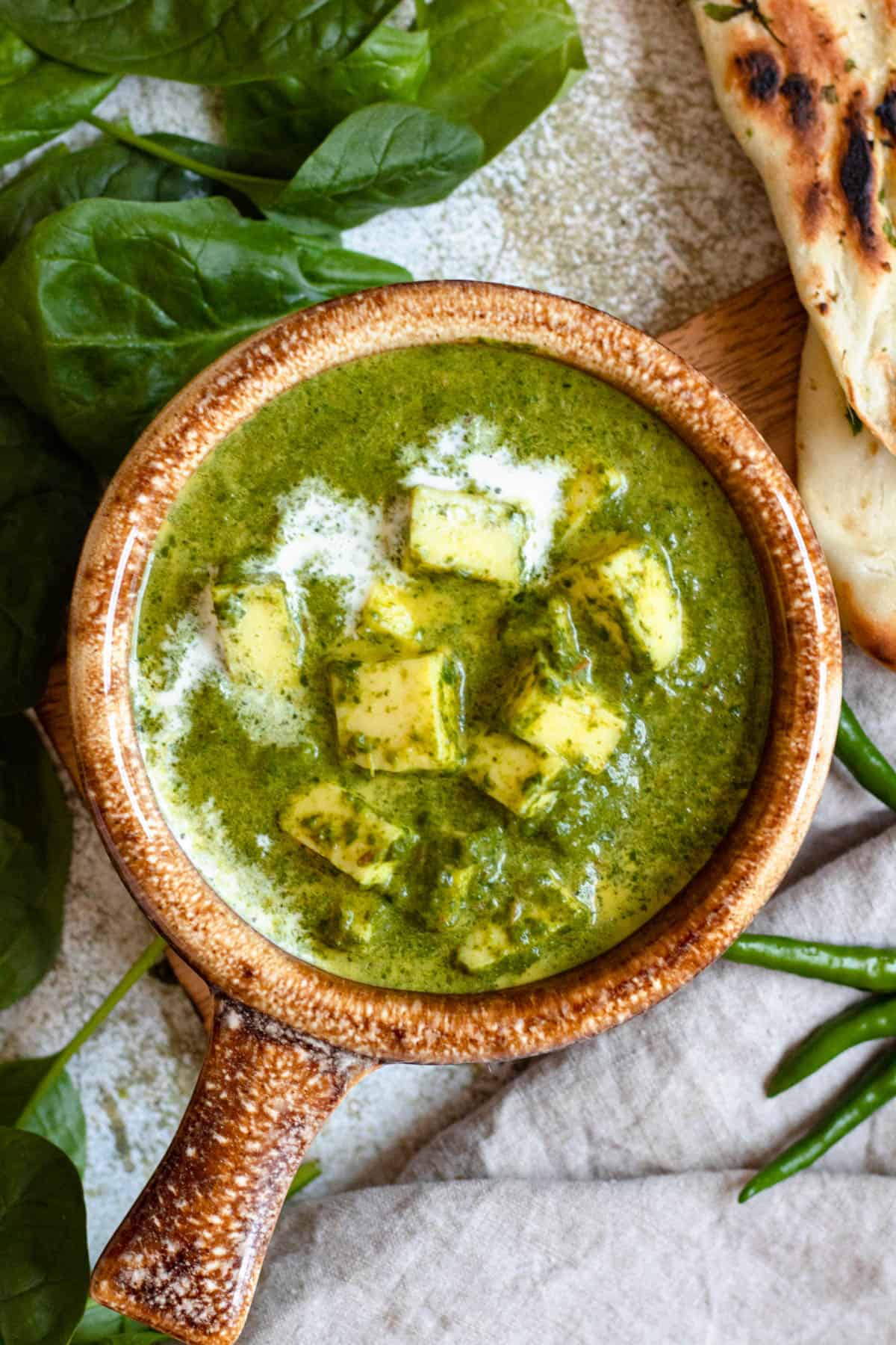 Crock of palak paneer with fresh spinach and green chilies garnished next to it. 