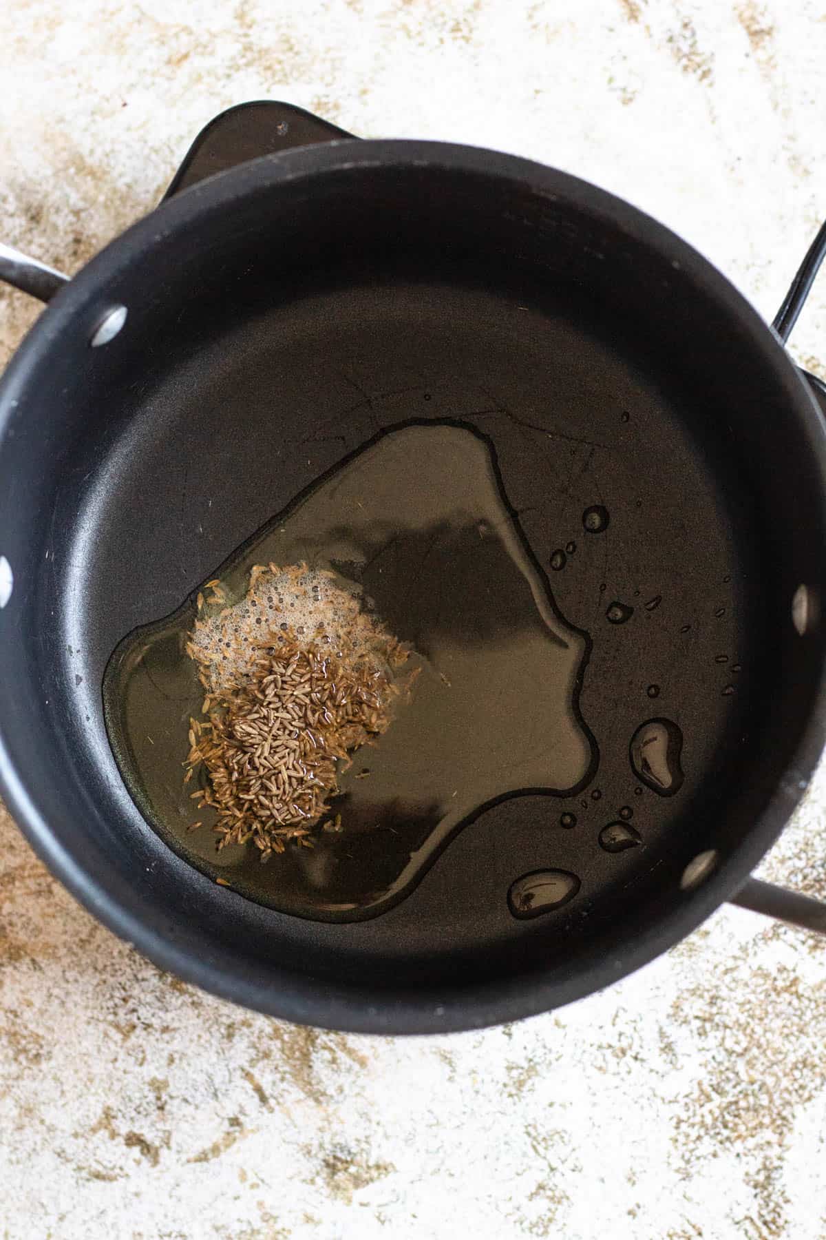 Spices added to hot oil in a saucepan. 