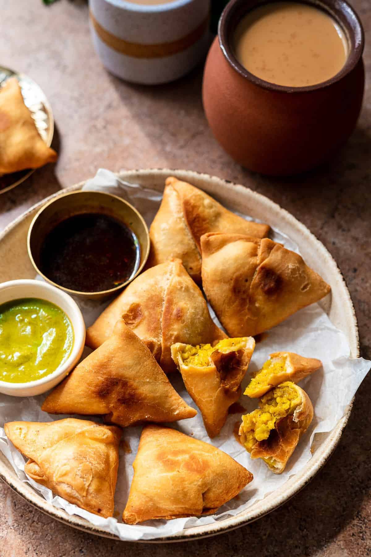 Paneer aloo samosas served on a plate with 2 dipping sauces in small bowls. 