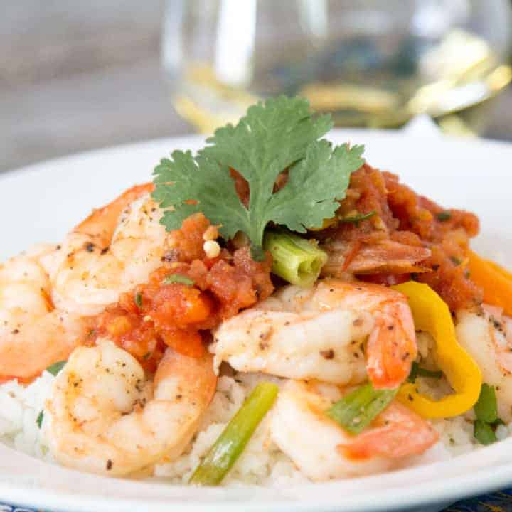 Baked shrimp with sweet peppers served over a bed of rice on a plate.
