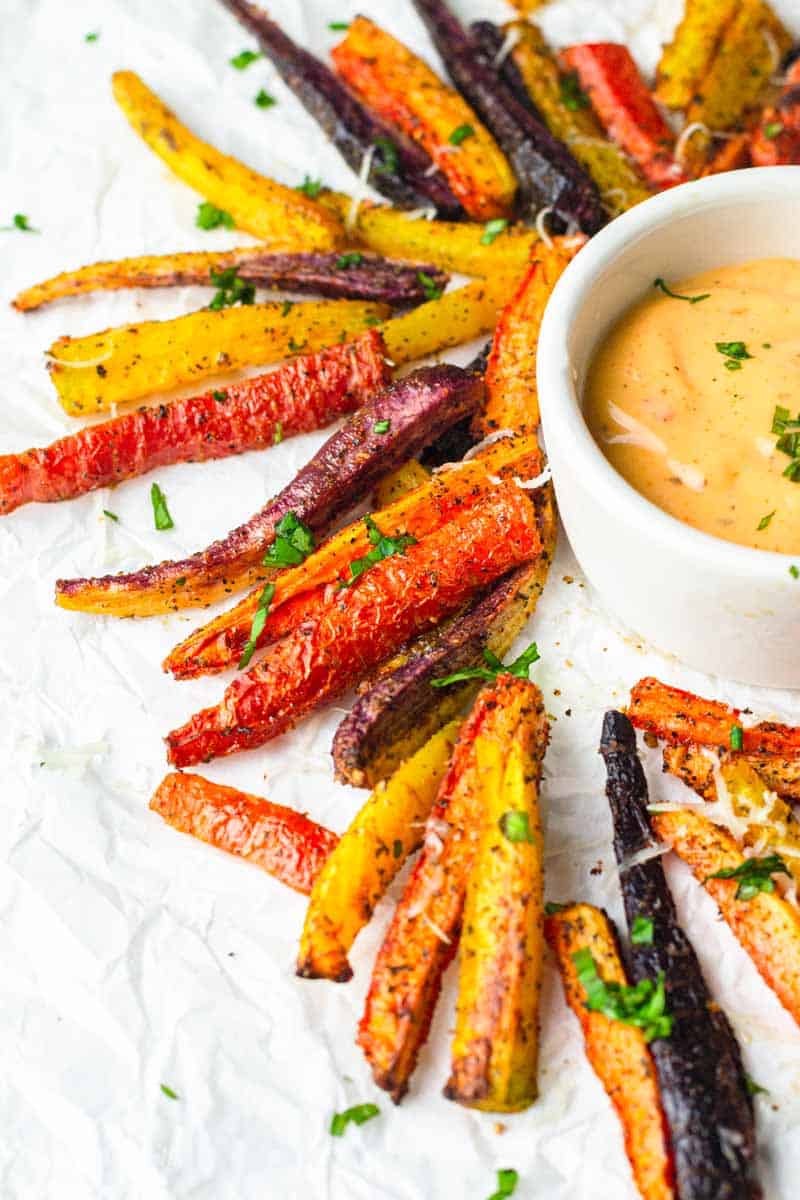 Air fryer carrot fries laying around a small bowl of dipping sauce. 