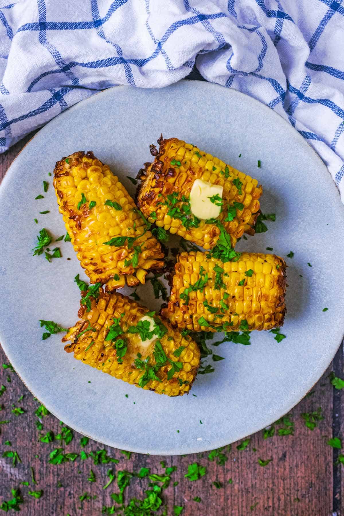 Air fryer corn on the cob served on a plate with a pat of butter melting into some of the cobs. 