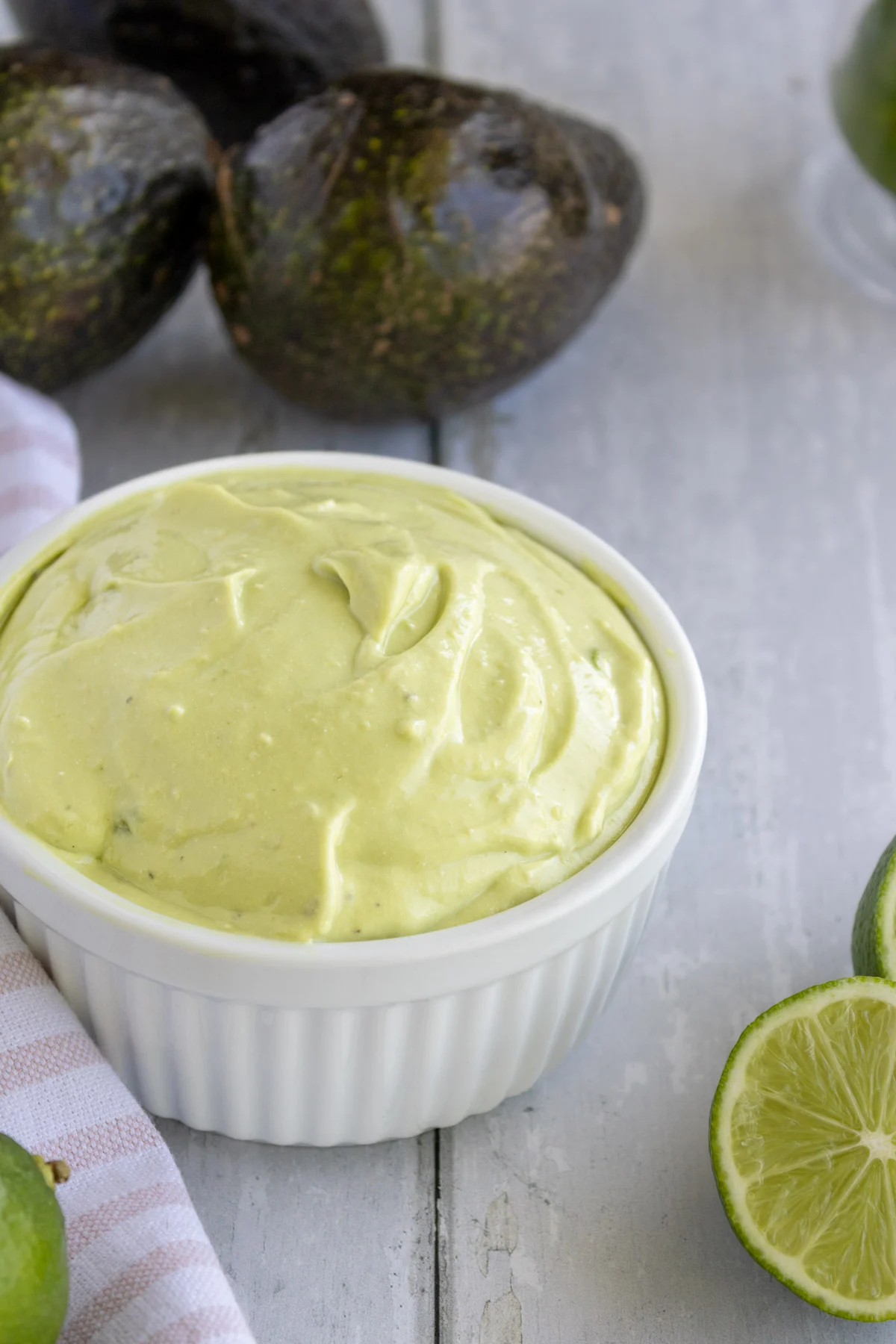 Small bowl of avocado crema with lime wedges and half an avocado next to it. 