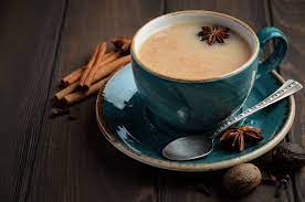 Blue tea cup with chai tea and an anise star garnished in it, on a saucer with a spoon resting on it. 