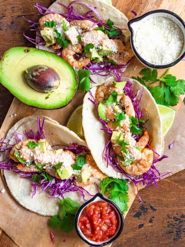 Top view of shrimp tacos with cilantro garnished on top and half an avocado on the side. 
