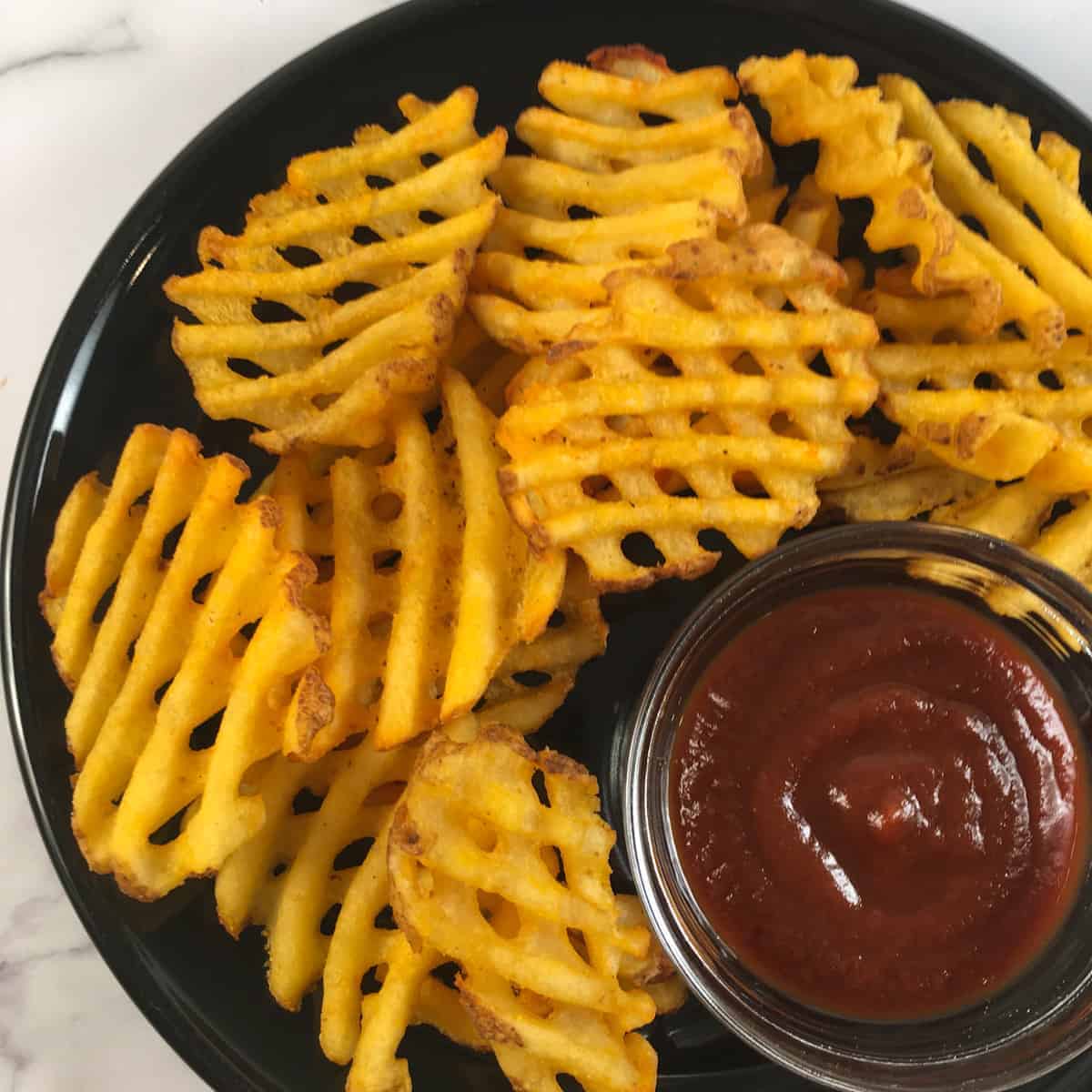 Waffle fries on a plate with a side of bbq sauce. 