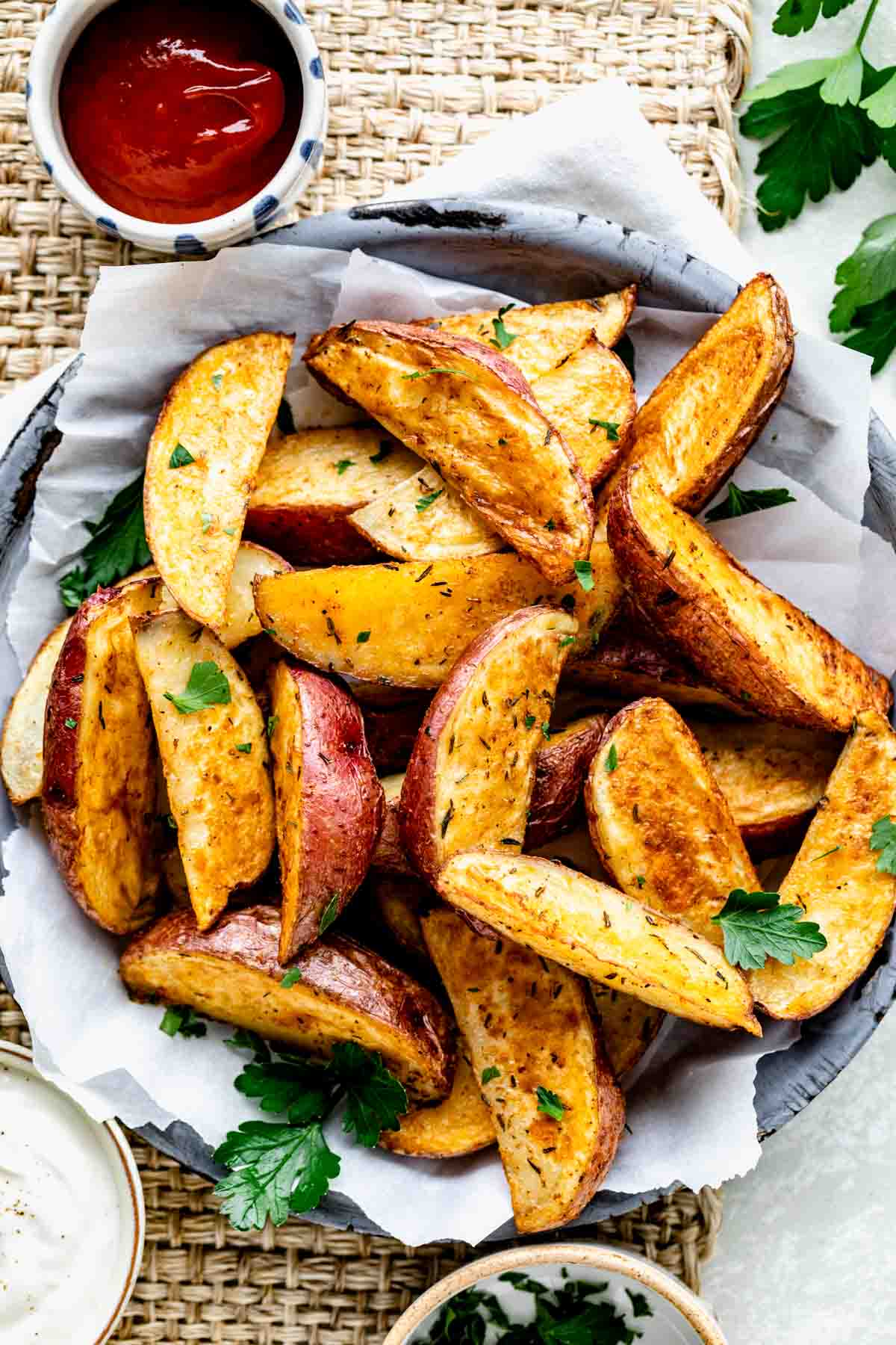 Oven roasted red potato wedges over parchment paper in a bowl and a small bowl of ketchup. 