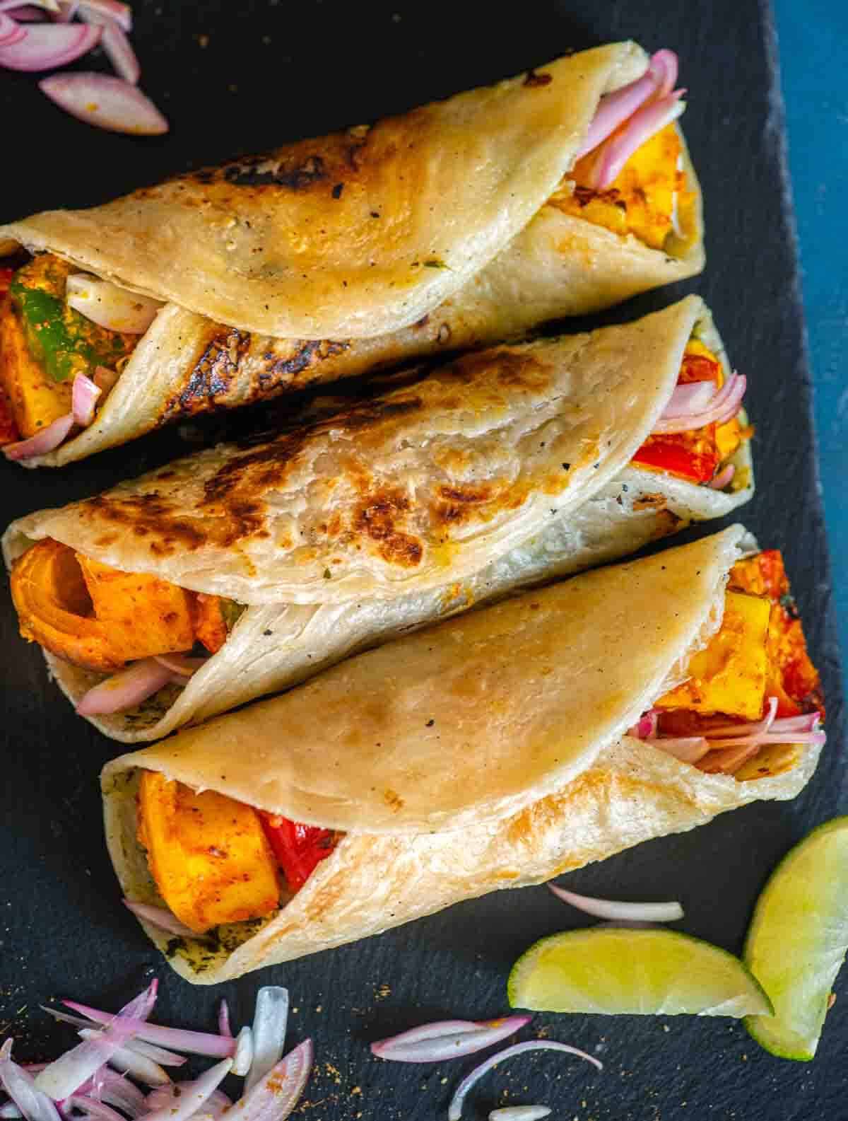 Paneer kathi rolls with lime wedges and red onion slices garnished on the side. 