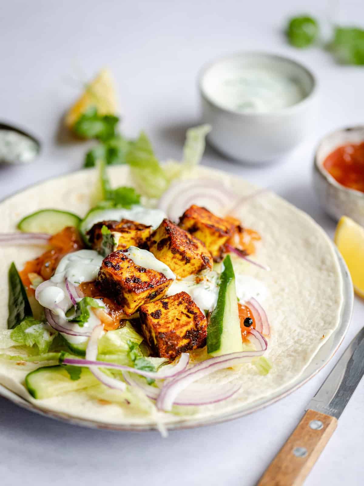 Spiced paneer wraps on a plate with a lemon wedge on the side. 