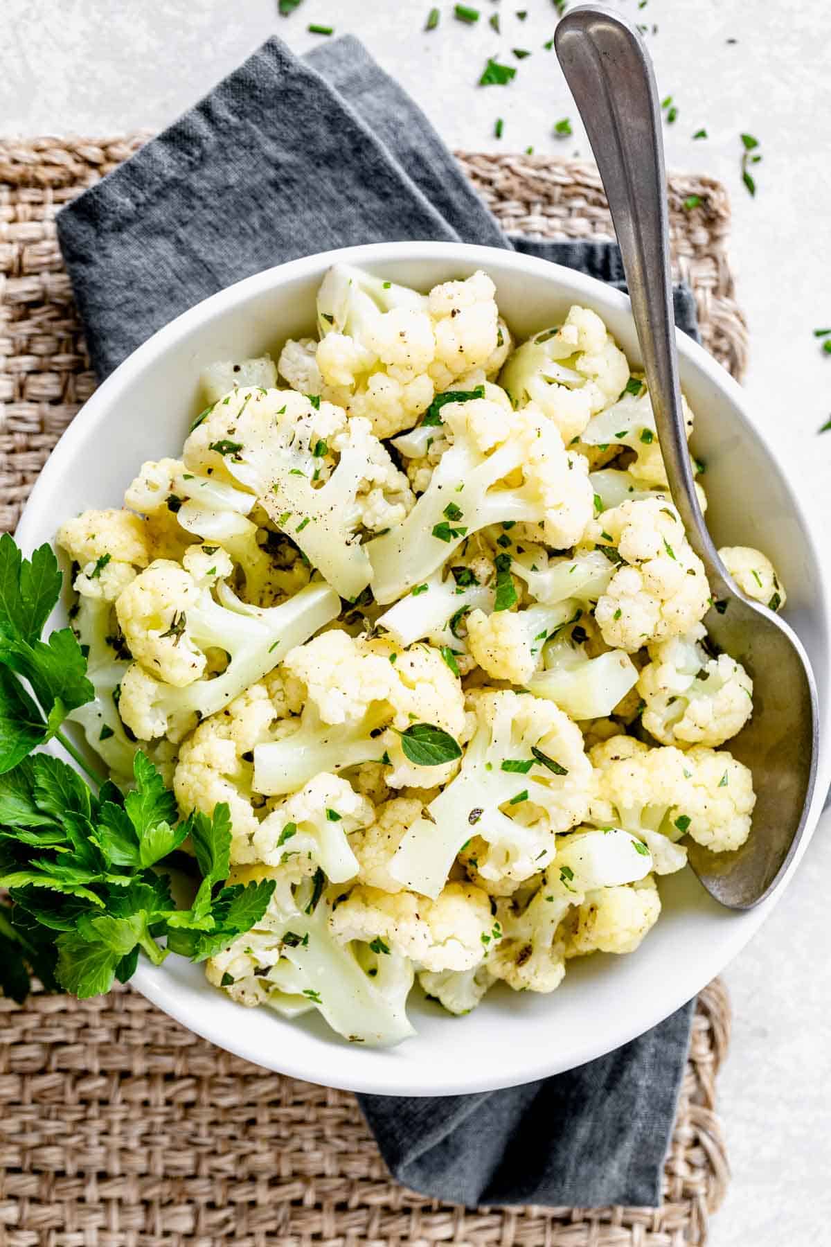 Steamed cauliflower with herbs in a bowl with a spoon resting in it. 