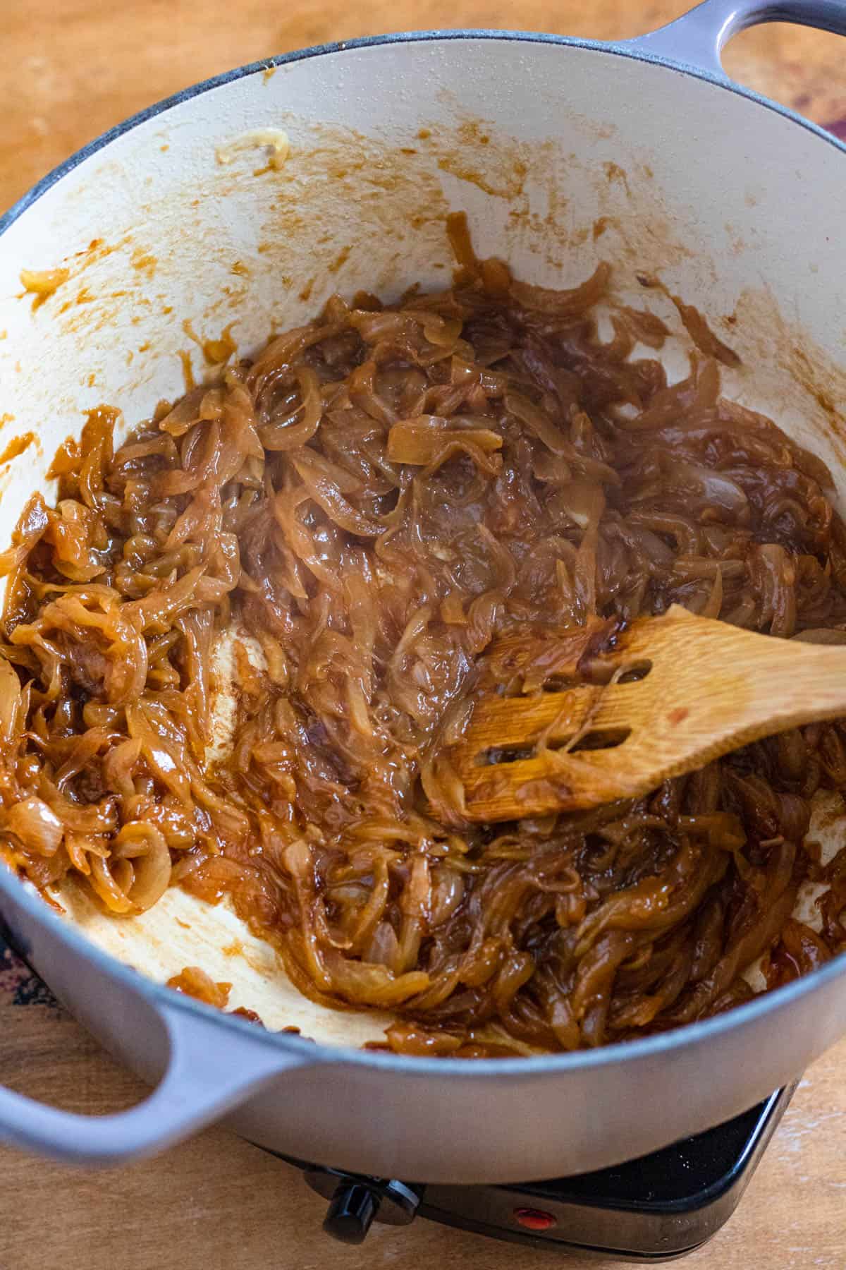 Wooden spoon stirring caramelized onions in a Dutch oven for a bowl of French onion soup. 