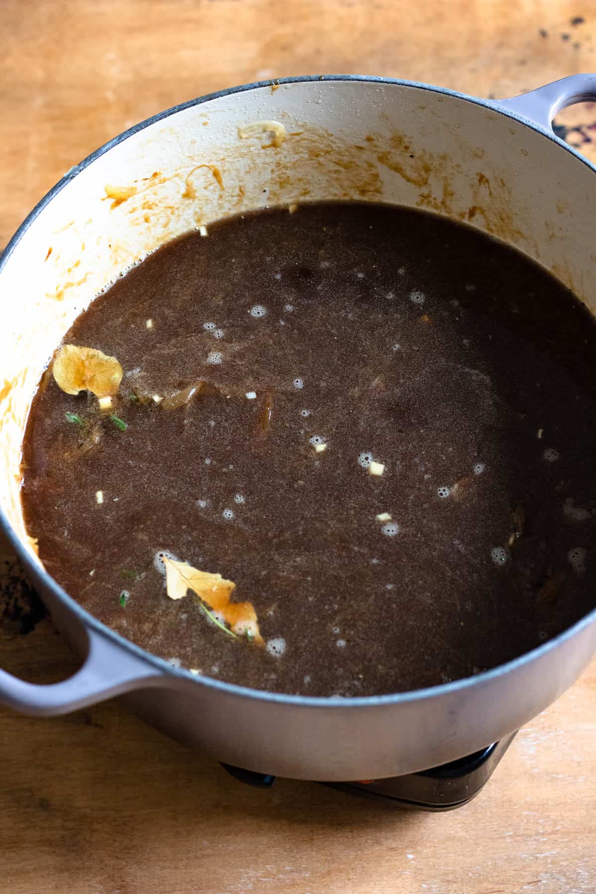 Broth and seasonings added to the caramelized onions in a Dutch oven to prepare for French onion soup.