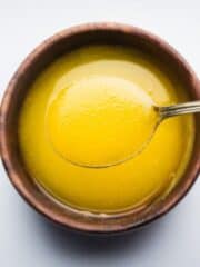 Ghee in a wooden bowl being scooped up by a spoon.