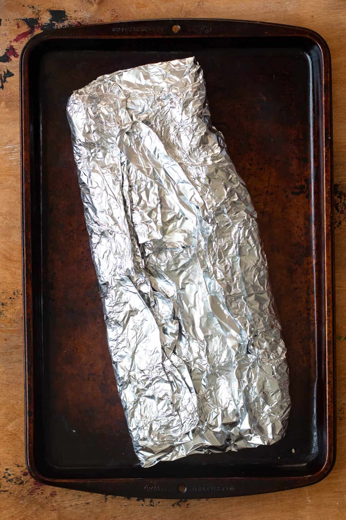 Nyama choma wrapped up in foil and laying on a baking sheet. 