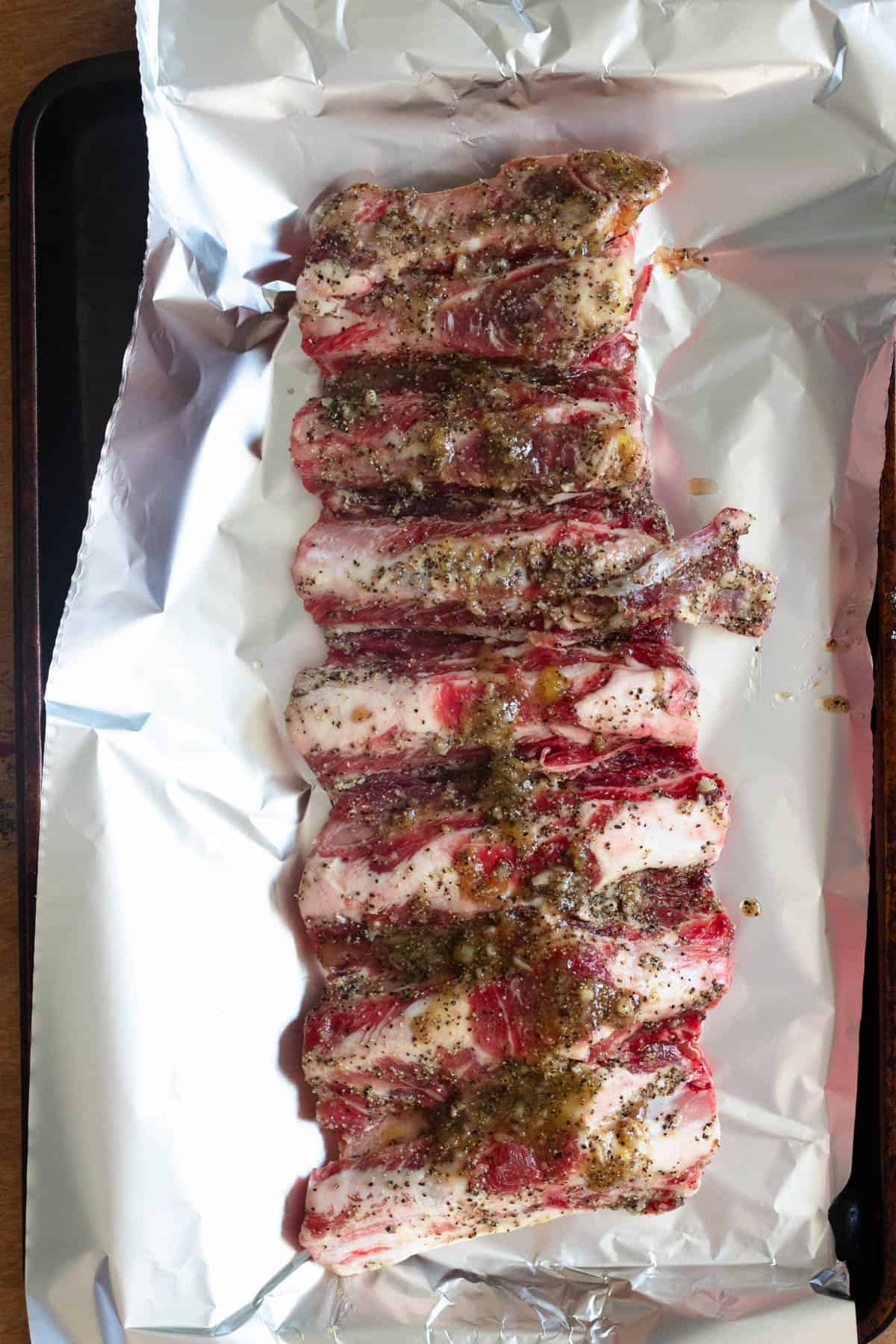 Nyama Choma marinated and on a piece of foil, sitting on a baking sheet, ready to be baked and grilled. 