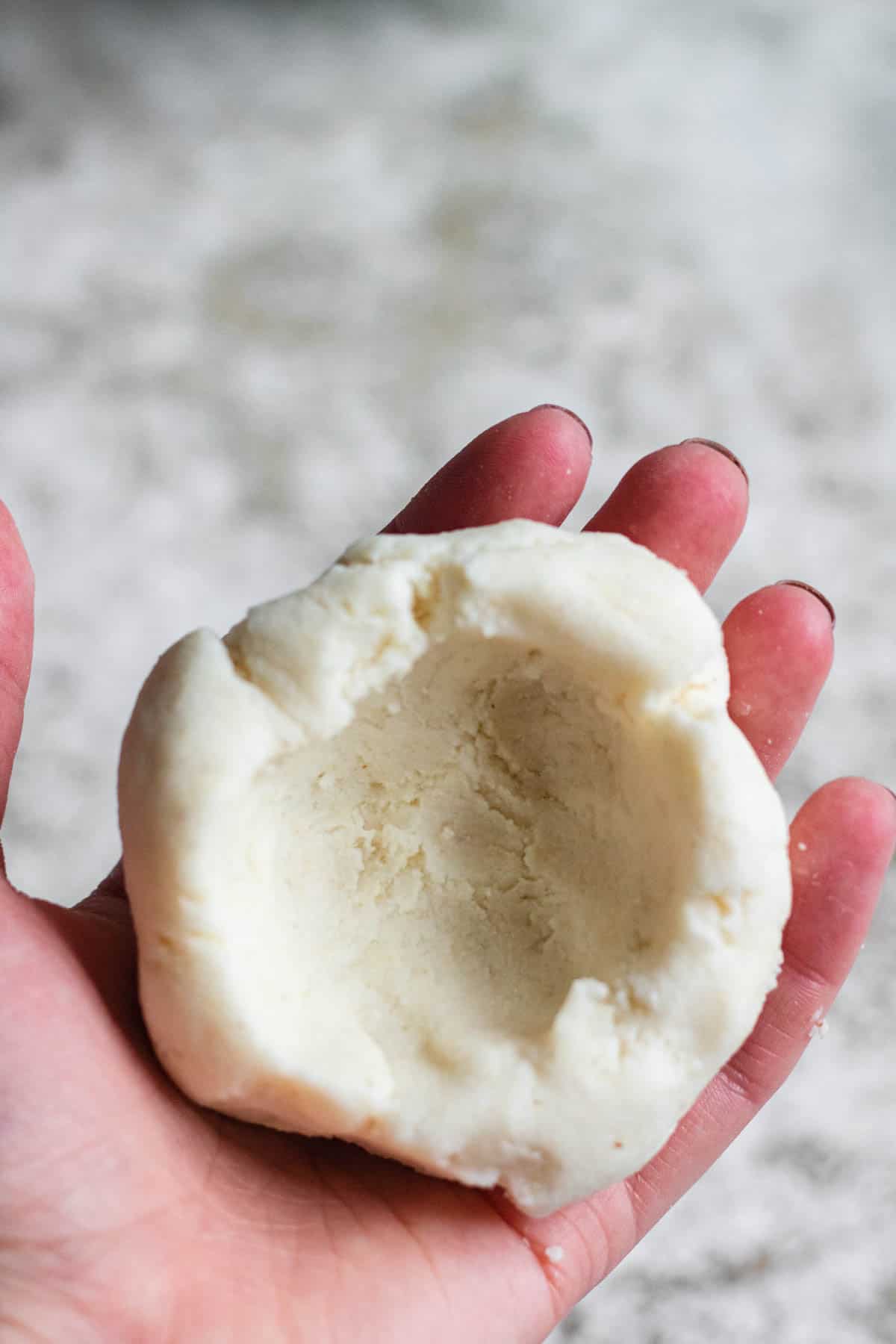Hand holding pupusas dough with a well made into it to place cheese. 