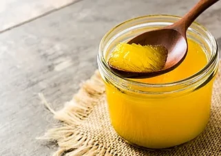 Small glass jar of ghee with a small wooden spoon of ghee being lifted out.