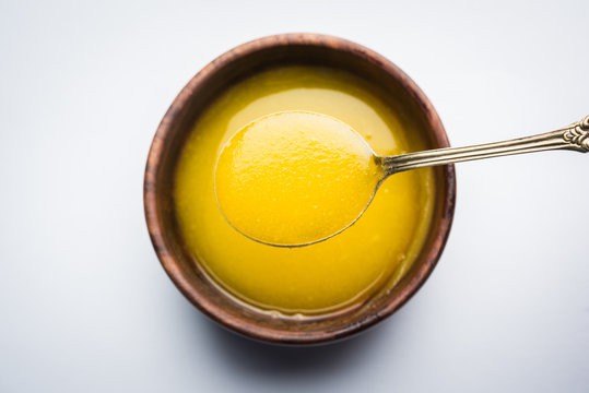 Bowl of ghee with a spoonful of it rising out. 
