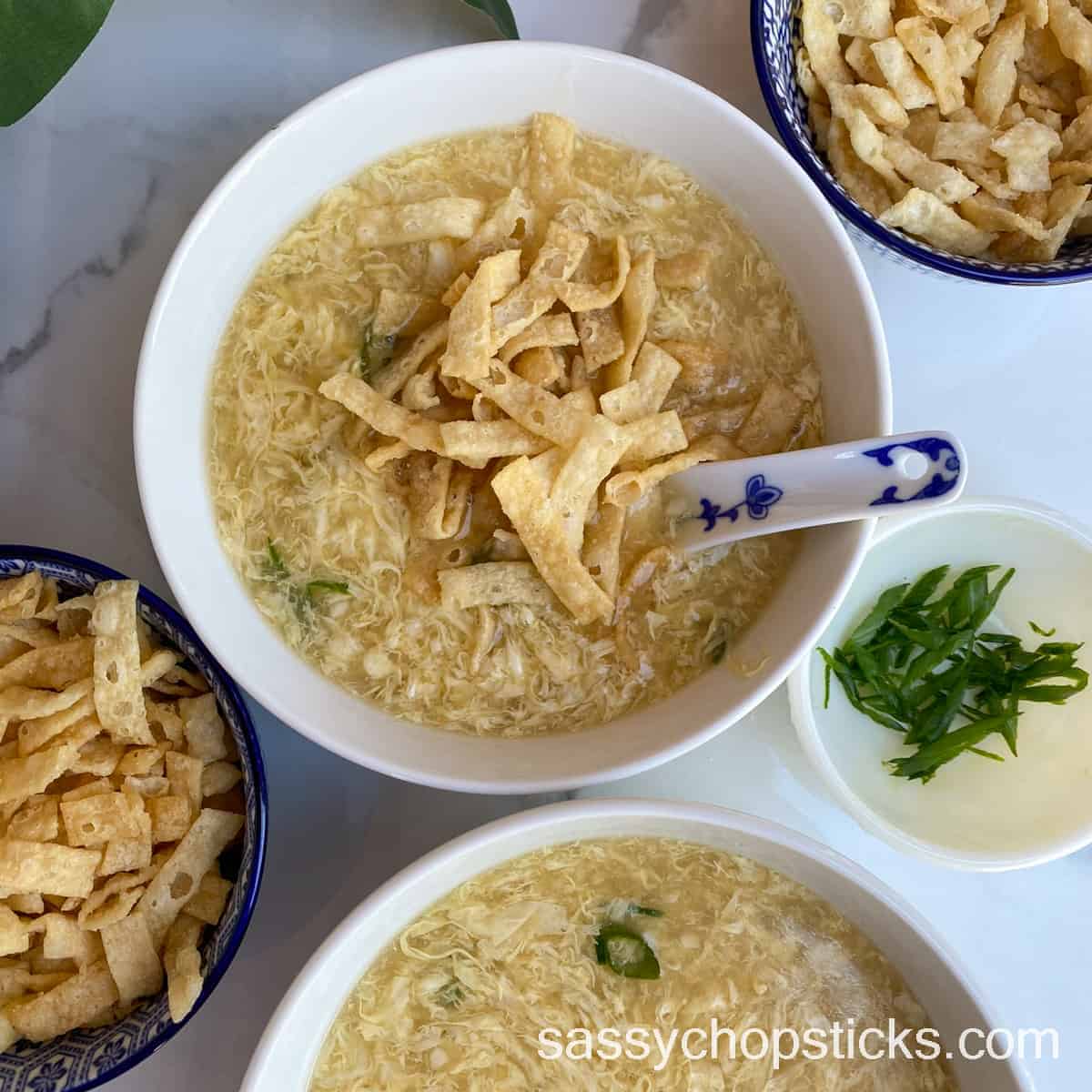 Egg drop soup served in a bowl with crispy pieces of wonton strips as a garnish on top. 