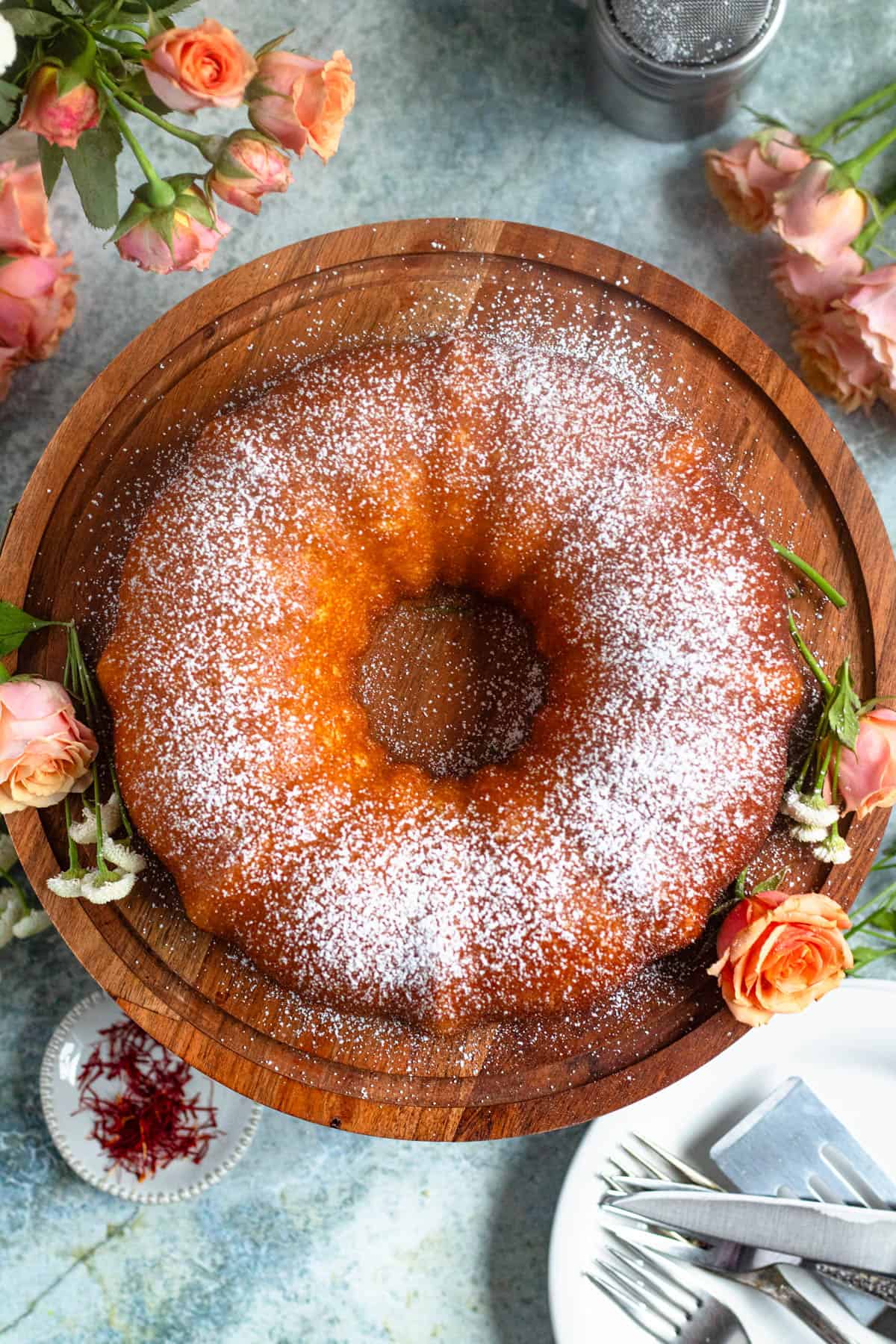 Top view of a baked cardamom cake dusted with powdered sugar and orange roses garnished on the side. 