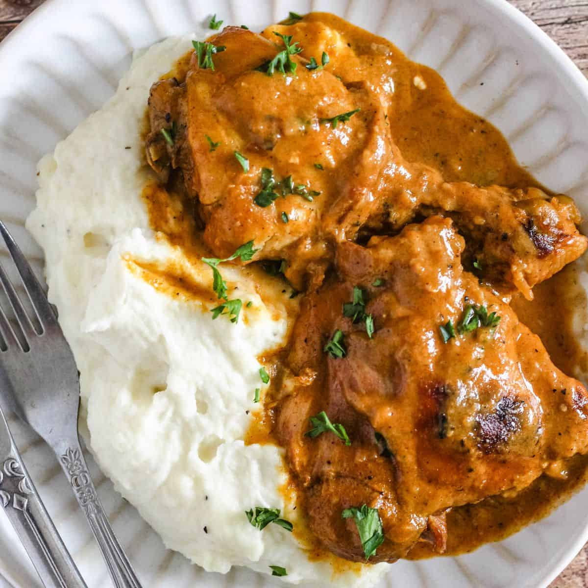 Plate of mashed potatoes with chicken paprikash served with fork and knife on the side.