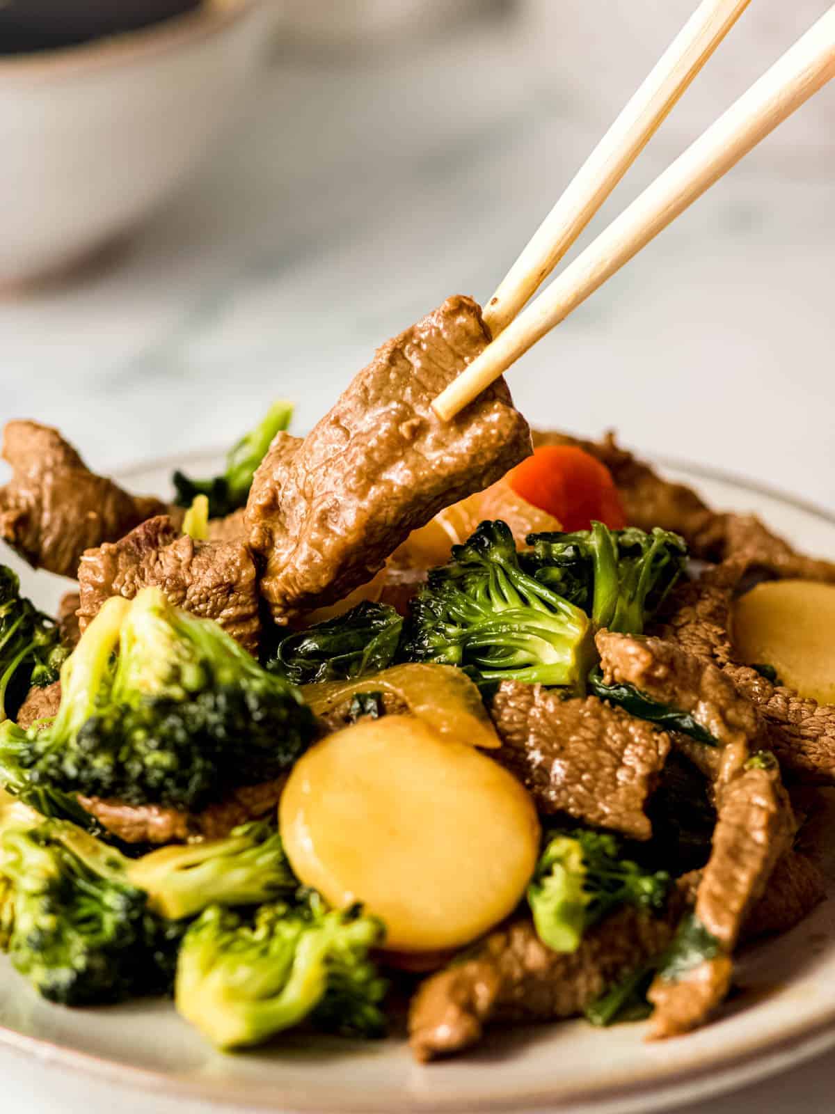 Chinese beef and vegetable stir fry on a plate with chopsticks picking up a piece of saucy beef. 