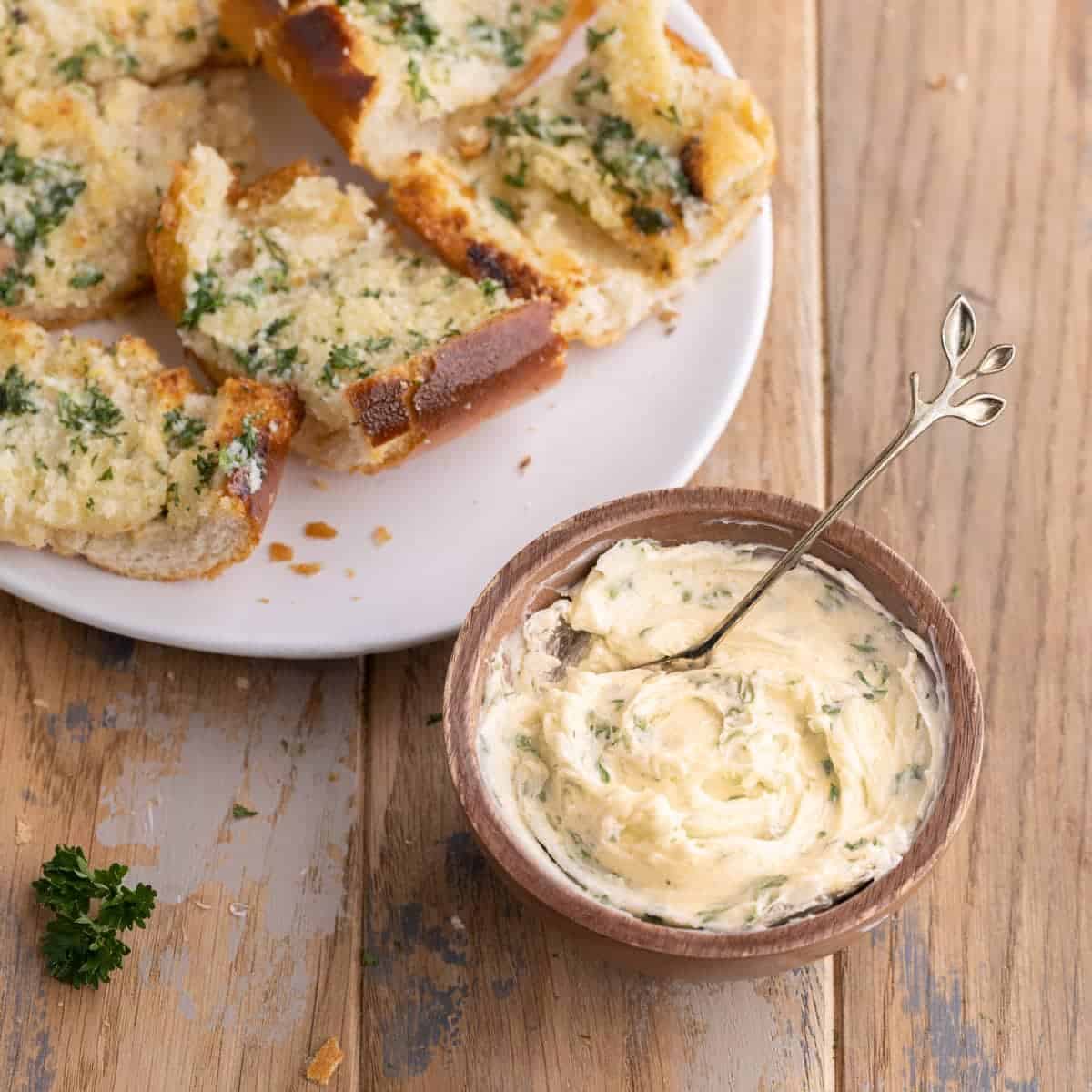 Garlic butter spread in a bowl next to toasted garlic bread slices. 