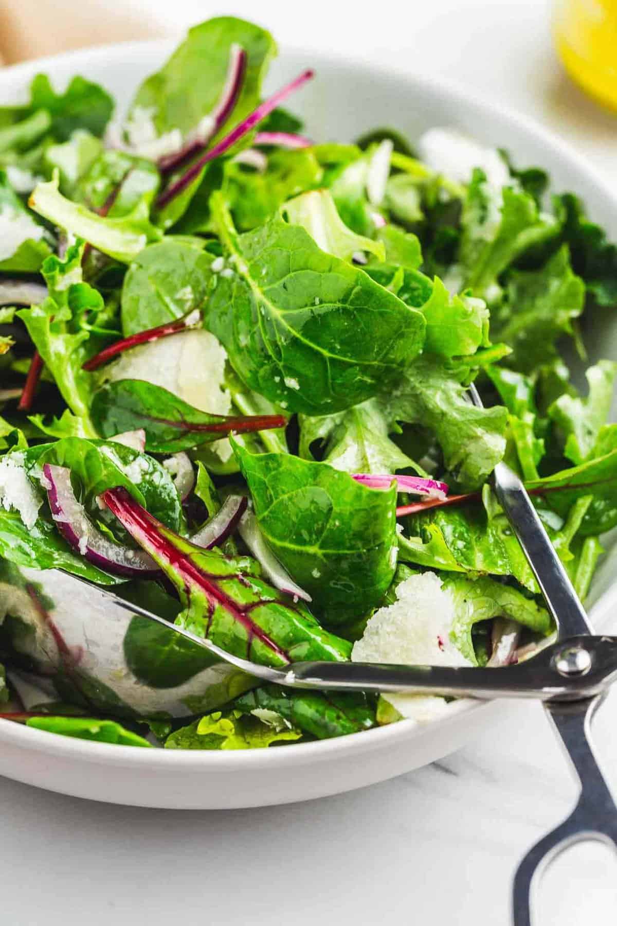 Simple tossed green salad in a salad bowl with metal tongs. 