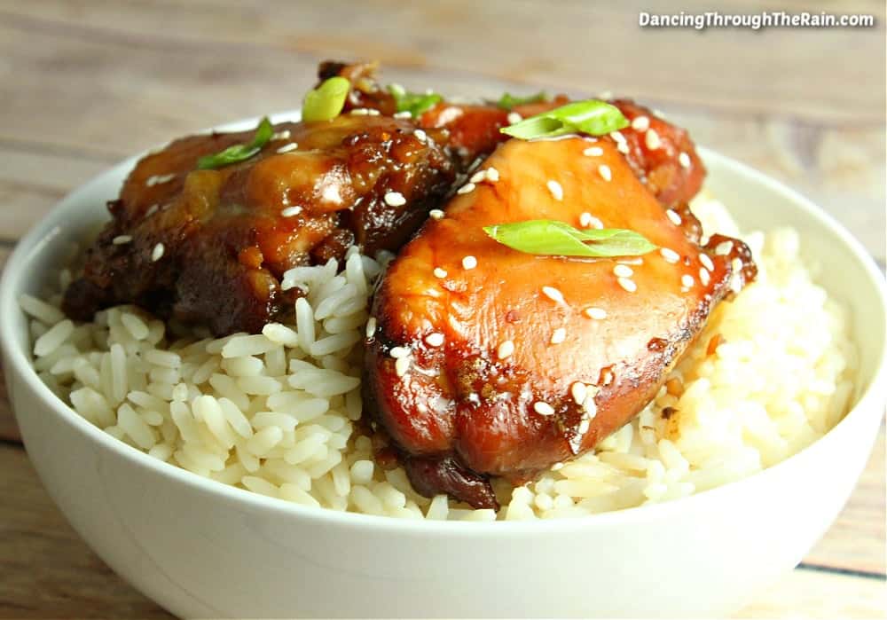 Slow cooker mongolian chicken with green onion slices over a bowl of white rice.
