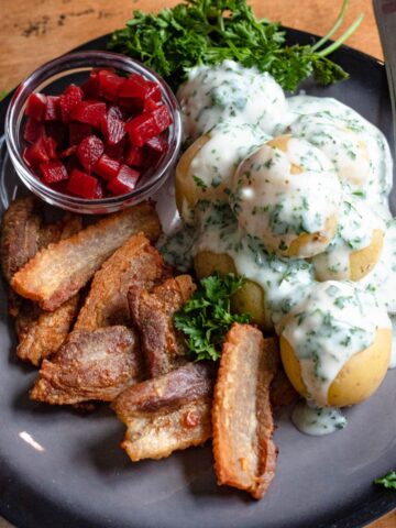 Stegt Flaesk on a dinner plate with potatoes, parsley sauce, and pickled beets