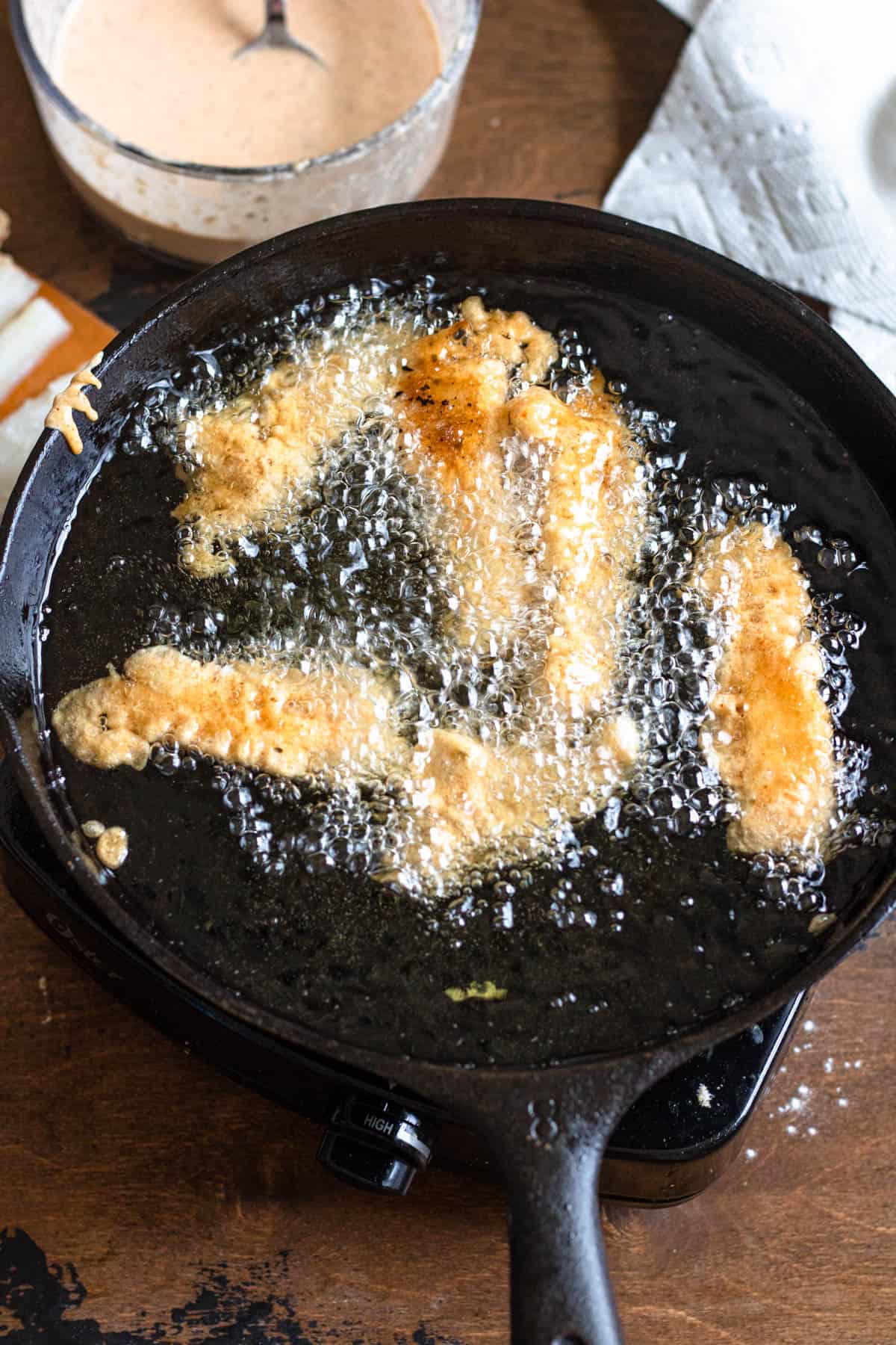 Cast iron skillet with fish sticks frying in it. 