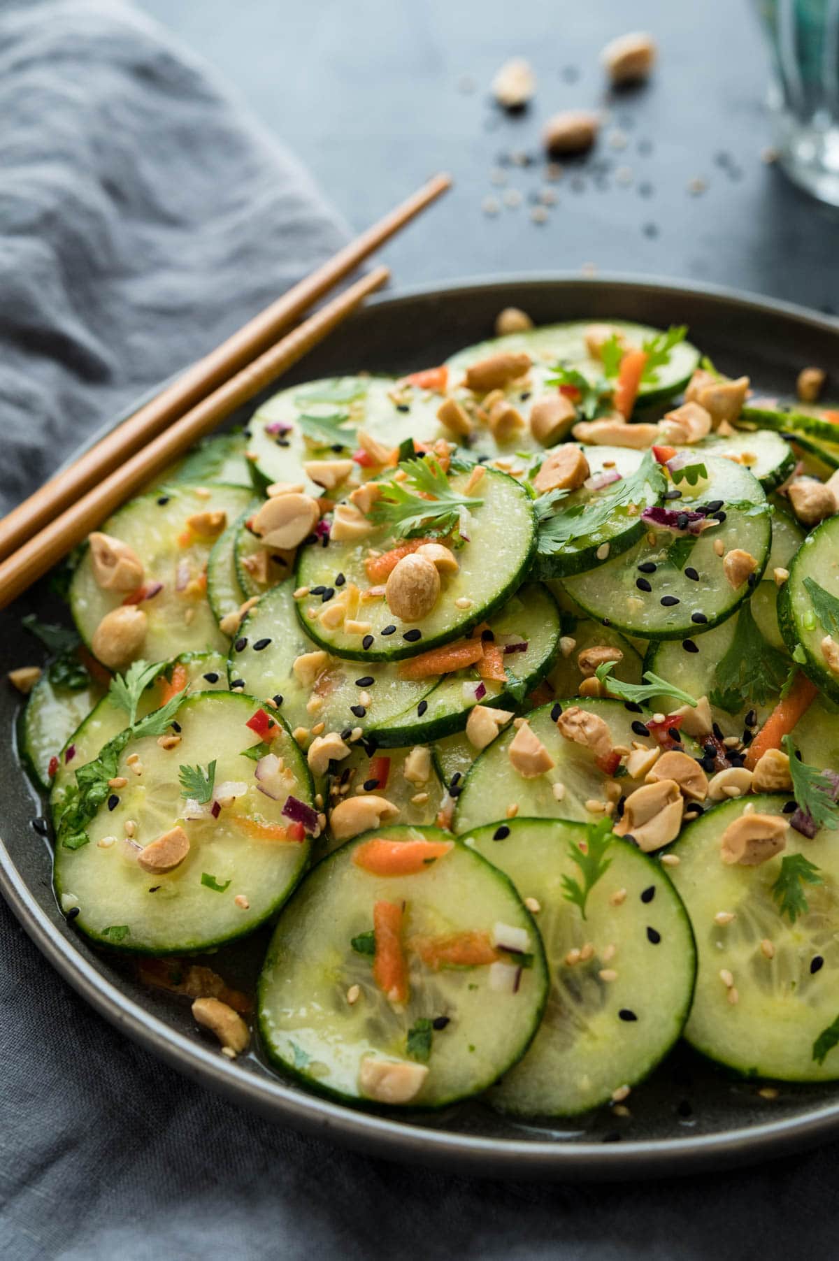 Asian cucumber salad with peanuts and sesame served in a bowl with chopsticks sitting on the edge.