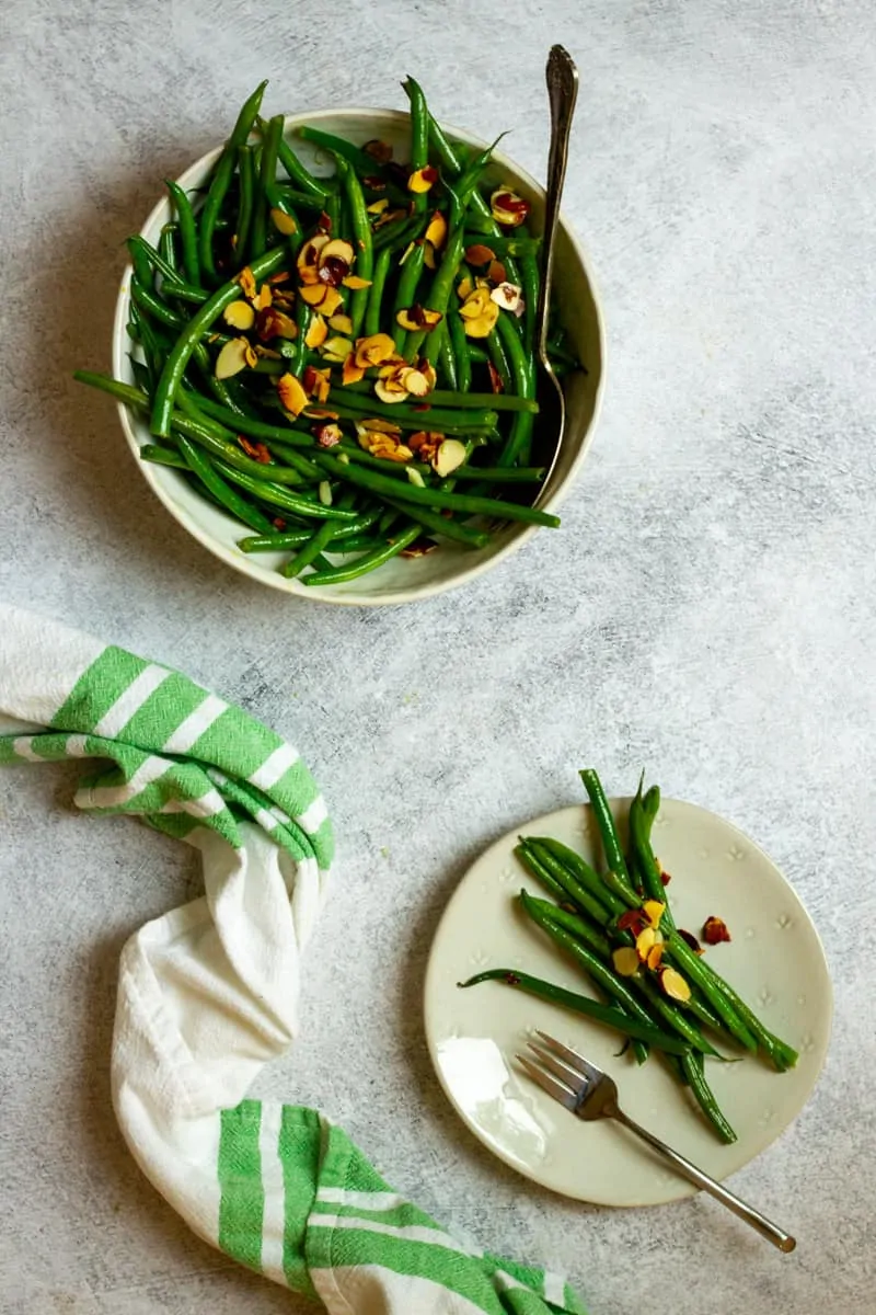Haricot vert salad with toasted almond slices on top, served in a bowl with a spoon resting in it. 