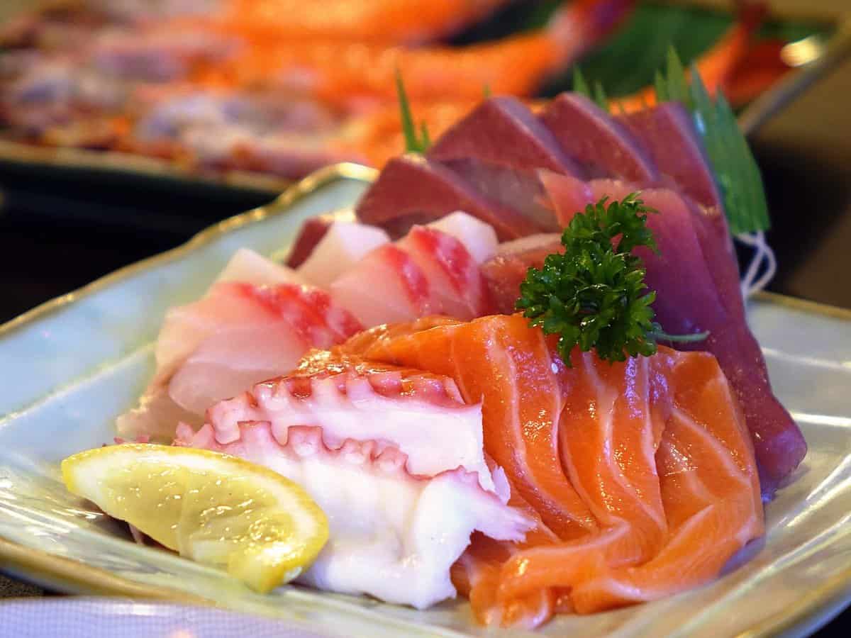 Sashimi slices of sushi grade meat served with a slice of lemon on the plate. 