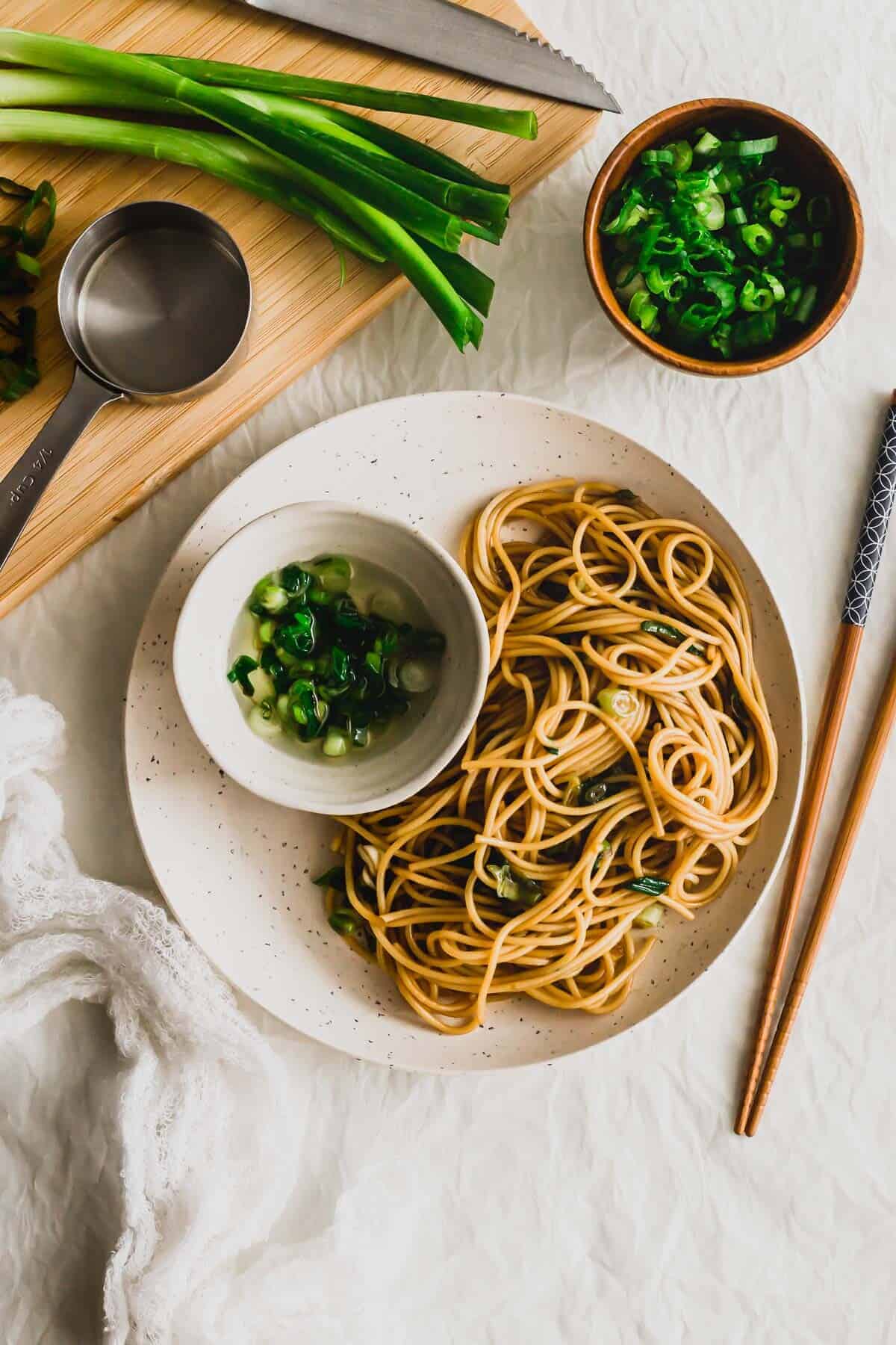 Quick and easy scallion oil noodles served on a plate with a small bowl of soup and chopsticks alongside the plate. 