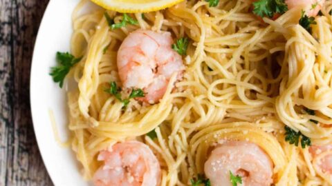 Partial top view of a plate of shrimp scampi prepared in the instant pot, served with a lemon wedge.