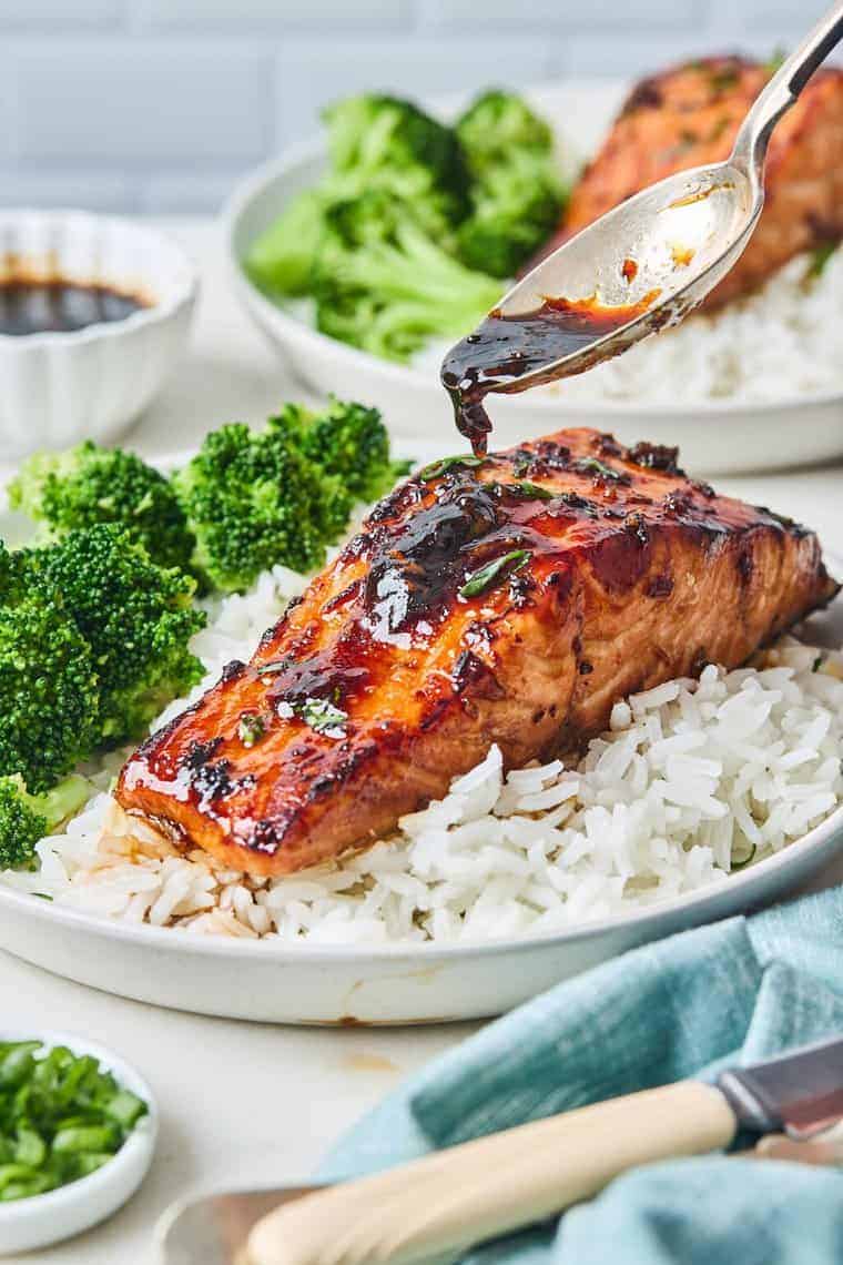 Air fryer salmon served over rice with a side of cooked broccoli and a spoon drizzling a honey garlic sauce over the top. 