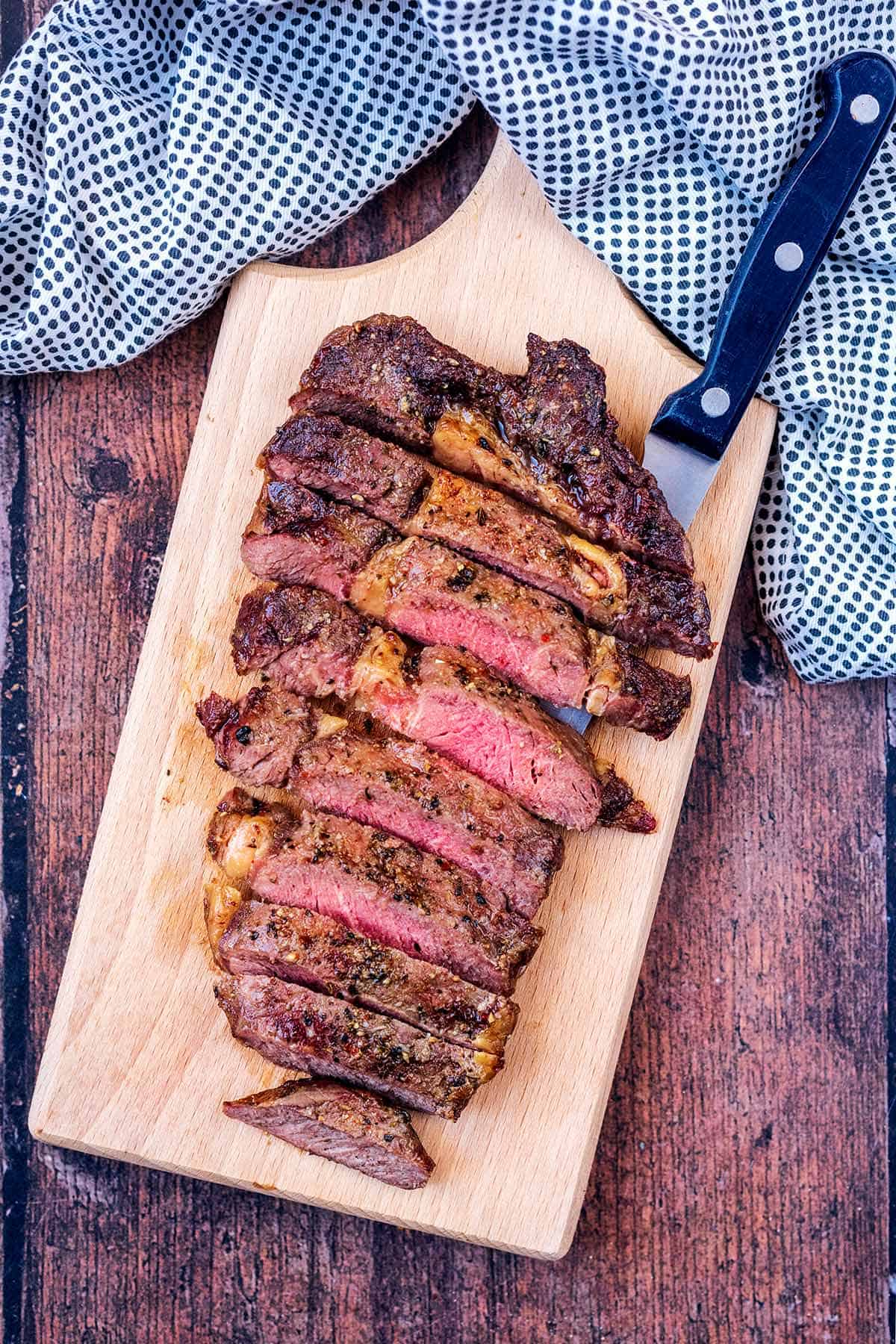 Air fryer steak cut into thin slices on a wooden serving board. 