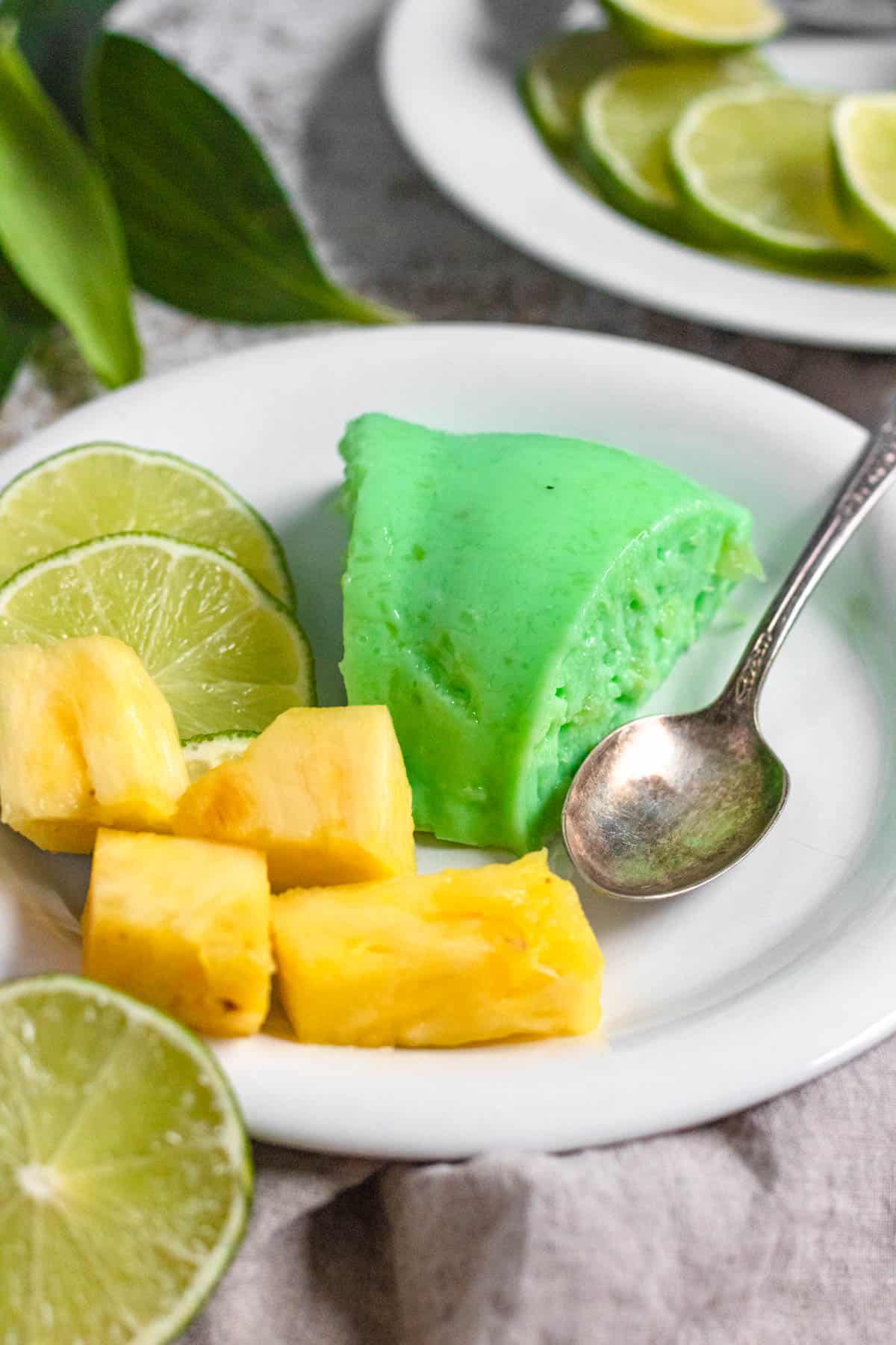 Slice of lime jello salad on a plate with lime slices and pineapple chunks. 