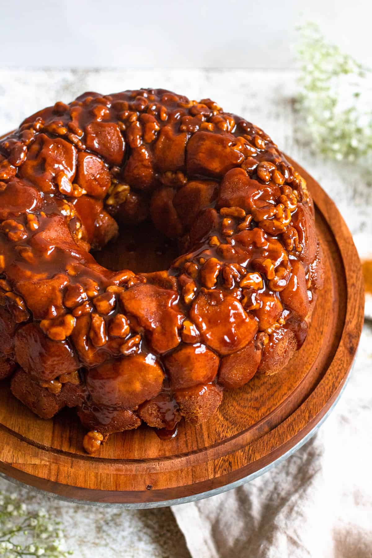 Monkey bread with caramel sauce over the top of the bread and pecans  sitting on a cake stand. 