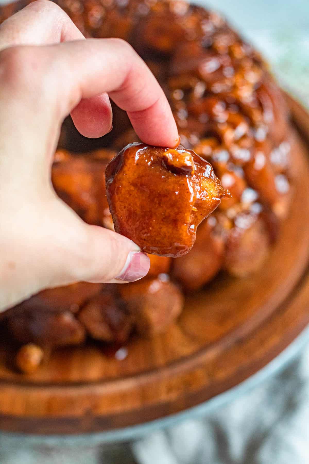Hand holding up a caramelized piece of monkey bread. 