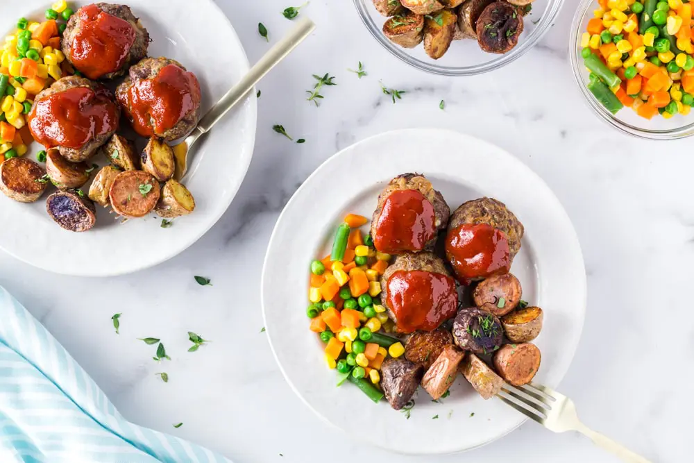 Onion burger meatloaf bites on a plate with mixed veggies and potatoes. 