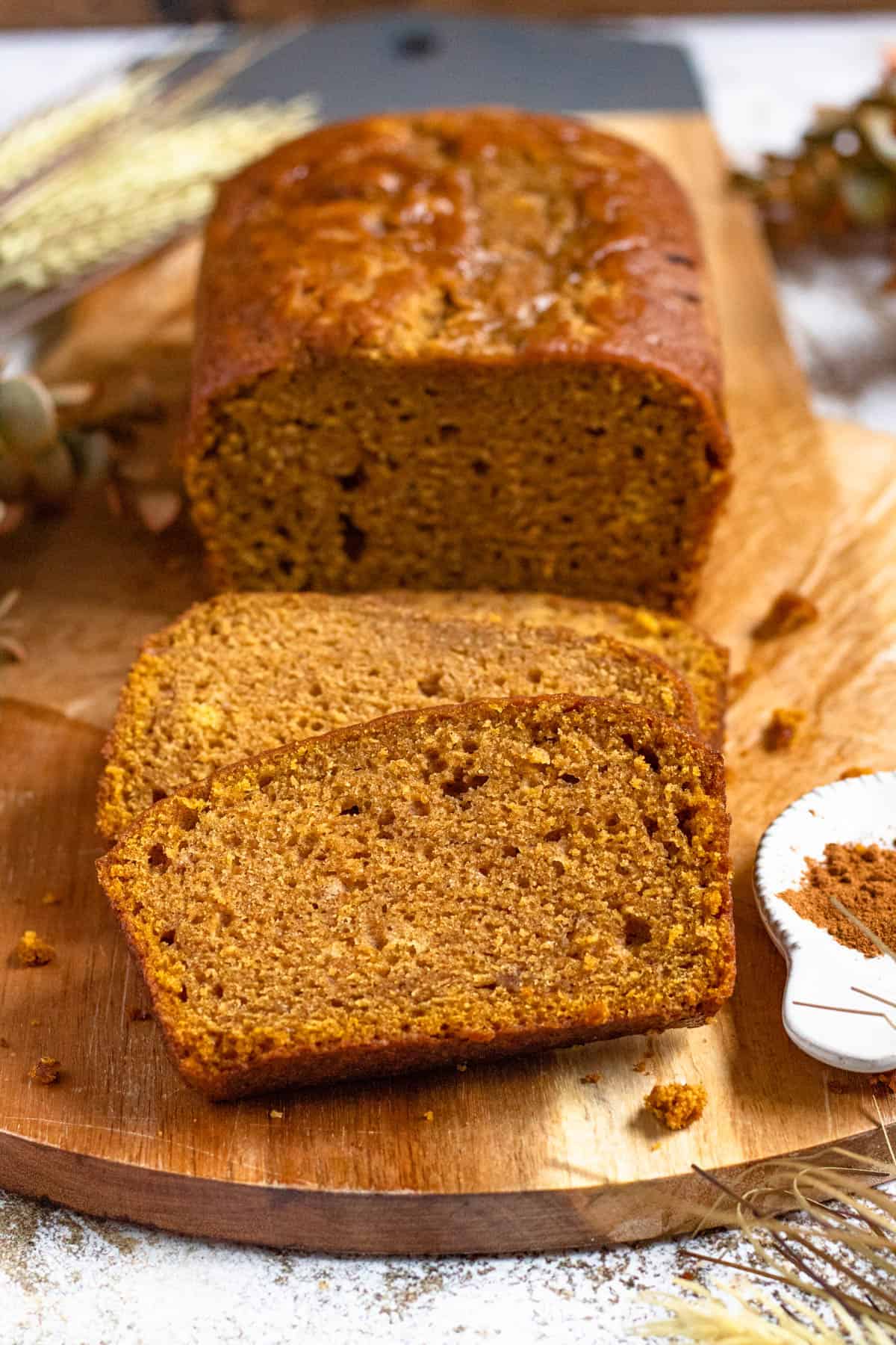 Golden pumpkin bread loaf with 3 thick slices cut off, laying in front, ready to serve. 