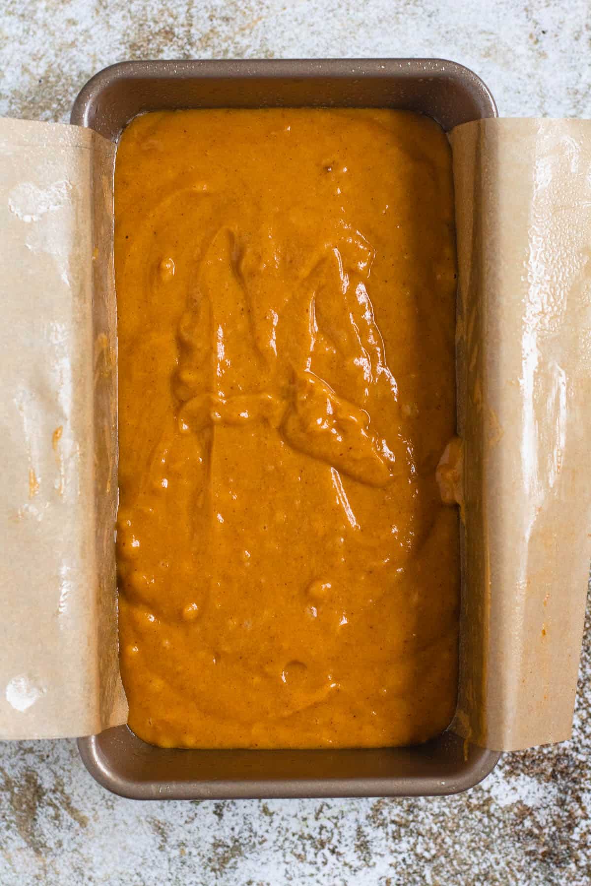 Pumpkin bread batter added to a parchment paper topped loaf pan, ready to bake. 