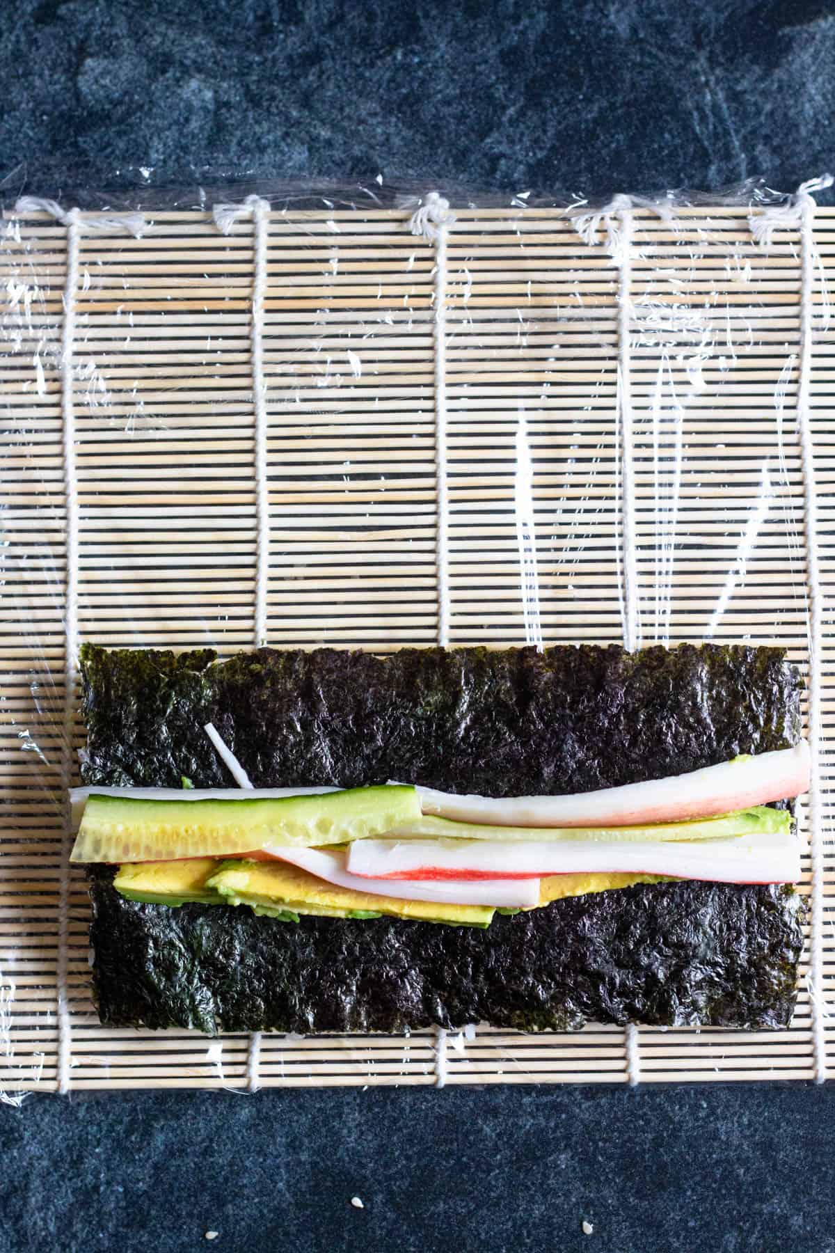 Nori sheet covering the sushi rice with thinly sliced cucumber, imitation crab and avocado slices. 