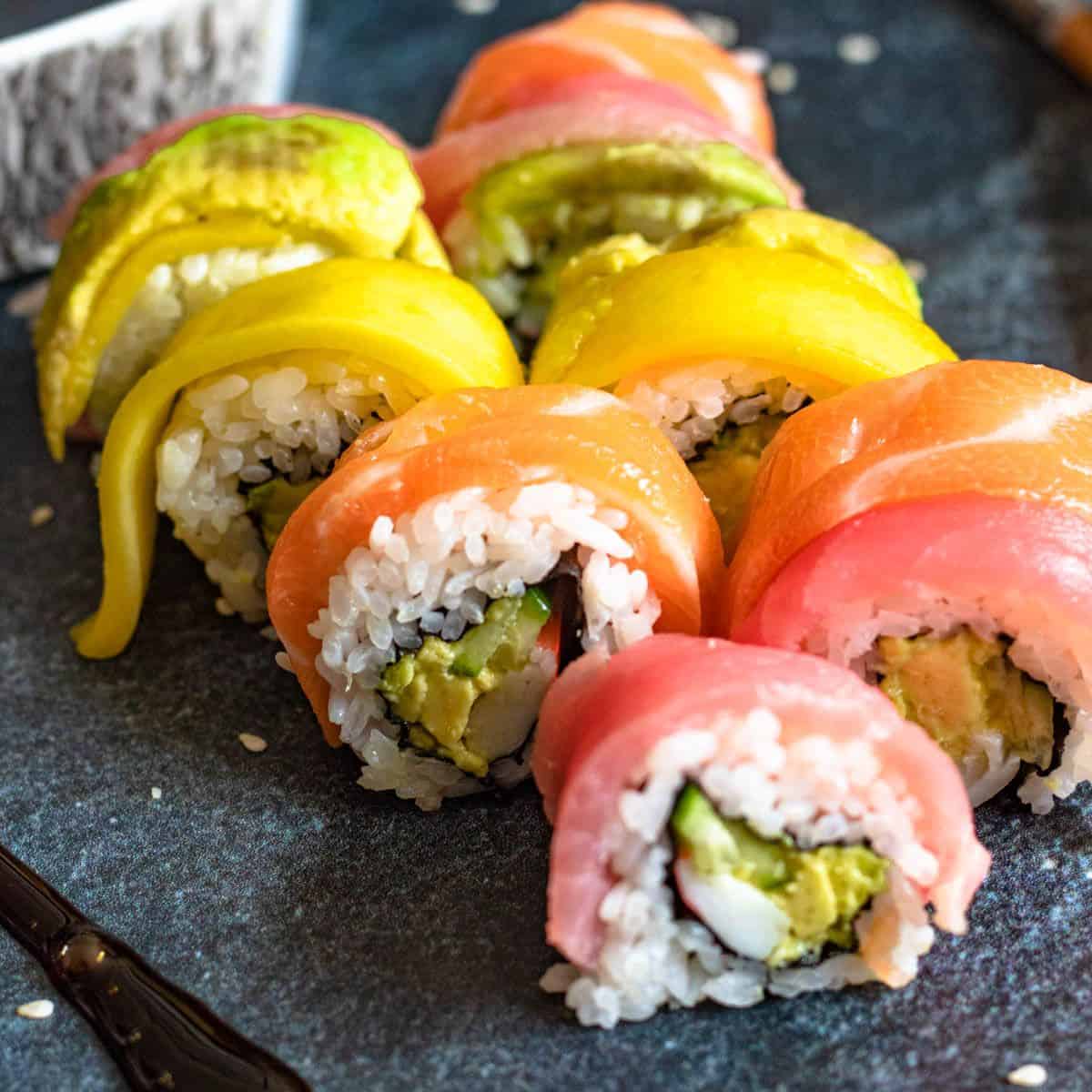 Slices of rainbow roll sushi topped with salmon, tuna, and avocado.