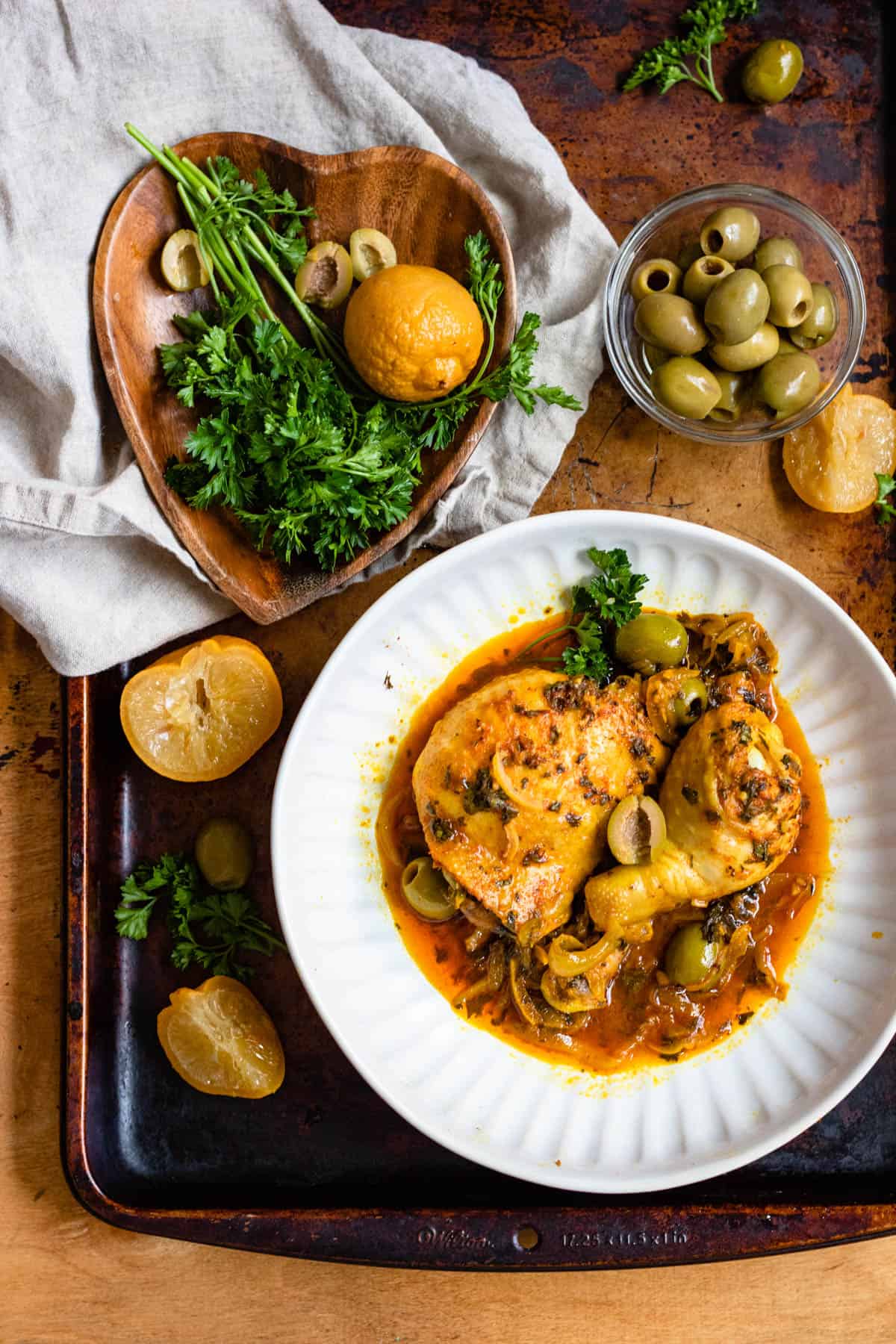 Plate of Moroccan Chicken Tagine Recipe with a small bowl of pitted green olives with half a preserved lemon garnished on the side. 
