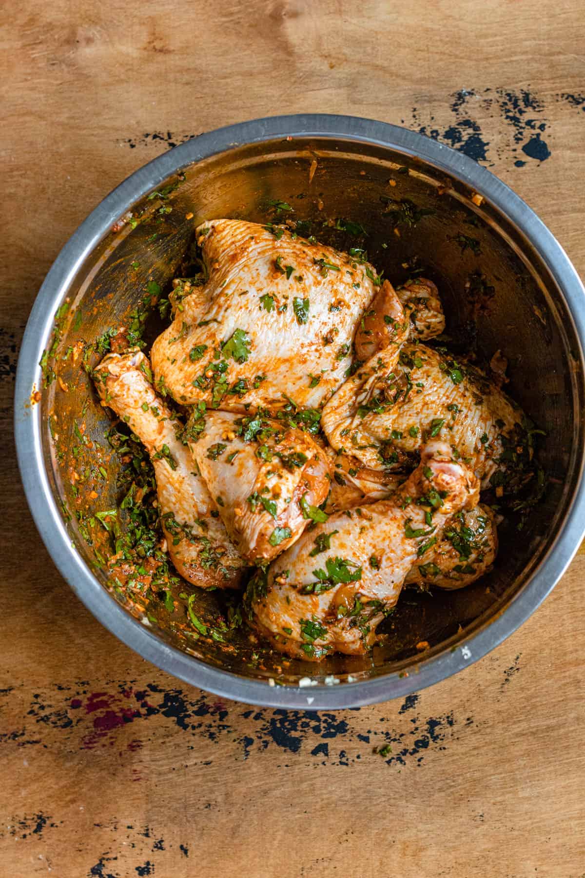 Bone in, skin on chicken covered in marinade in a mixing bowl on a Moroccan chicken tagine recipe. 