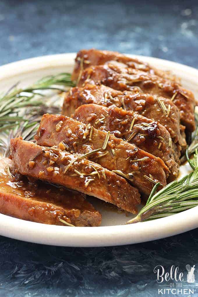 Slices of honey dijon pork tenderloin resting on a serving plate with fresh herbs garnished. 